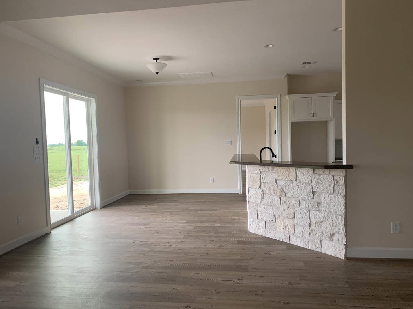 Open kitchen with stone countertop, black faucet, wood flooring, stone accent wall, large window overlooking field, ceiling light fixture