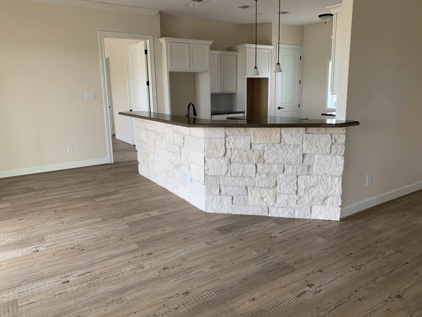 Open kitchen and dining area featuring white stone walls, black sink, wood flooring, marble countertops, white door, and modern lamp.