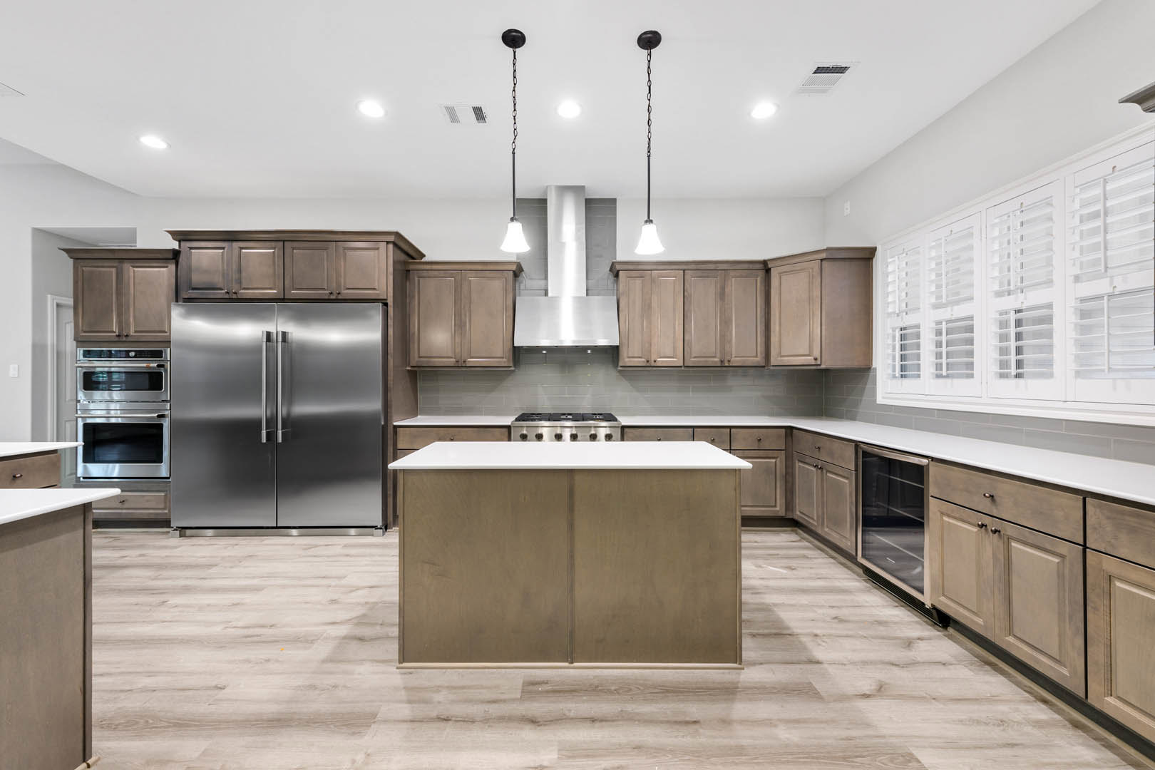 Open-concept kitchen featuring a stainless steel refrigerator with double handles, white cabinetry, quartz island countertop, stainless steel oven, white shutters along the wall