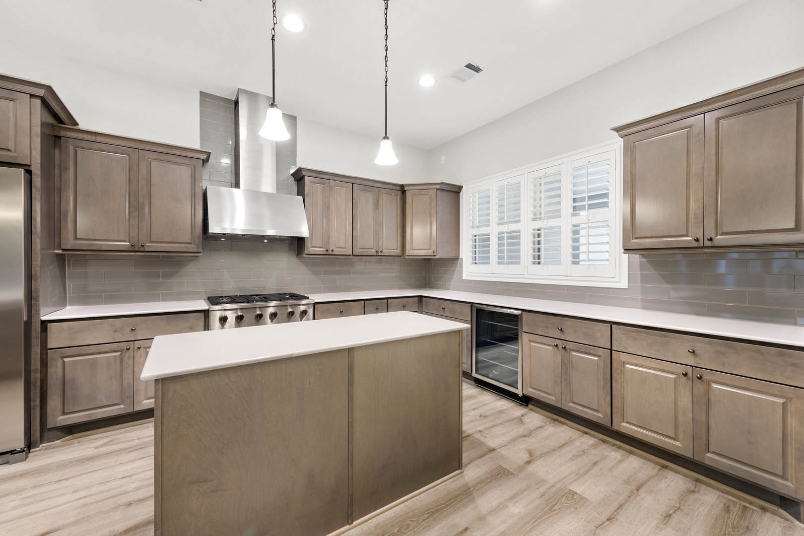 Kitchen with wide plank wood flooring, large central island with white cabinetry, stainless steel stove and oven, white cabinets, glass door, and row of white windows with