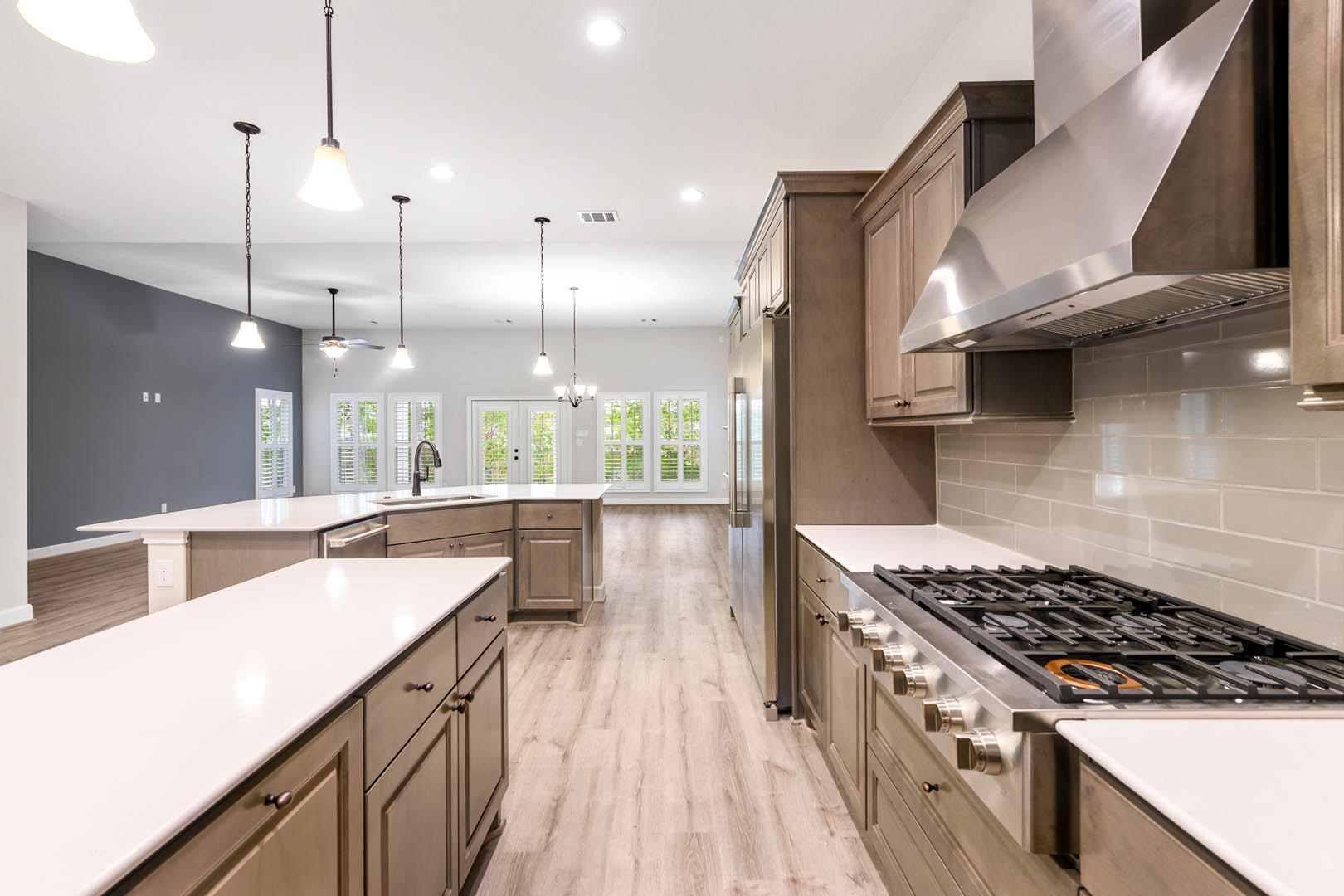 Spacious kitchen featuring a large white island with drawers, stainless steel stove top, tile backsplash, white cabinetry, pendant bell light fixture, and light wood flooring.