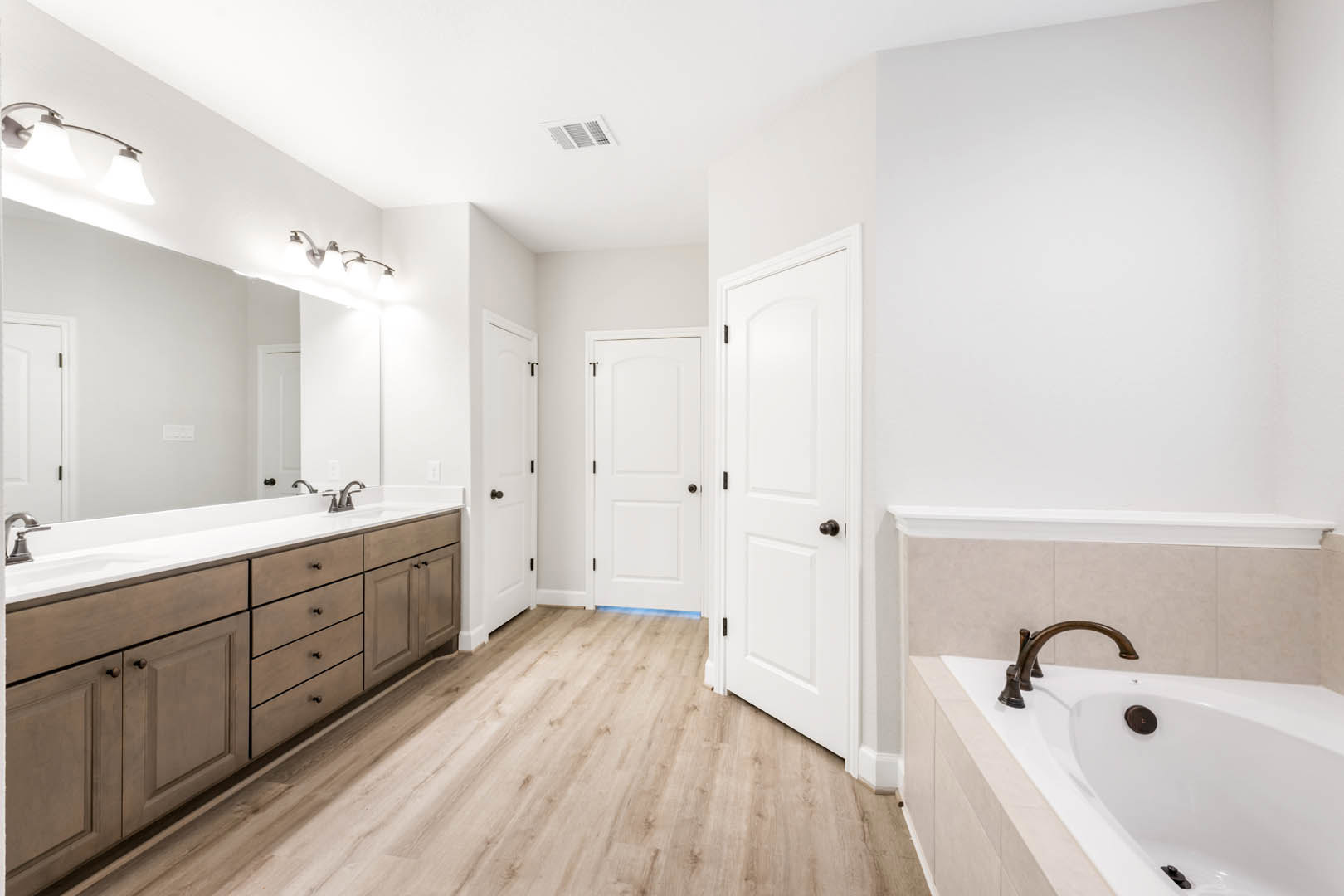 Modern bathroom featuring a freestanding white bathtub, sleek undermount sink with chrome faucet, white paneled door with black hardware, light gray tile flooring, and white