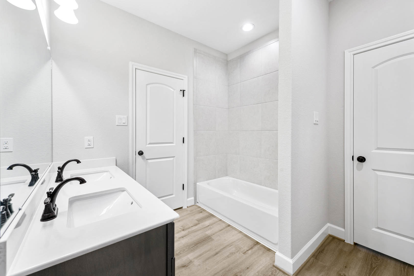 Modern bathroom featuring a freestanding white bathtub, rectangular sink with chrome faucet, light gray tile walls, white door, and white electrical outlet and light switch.