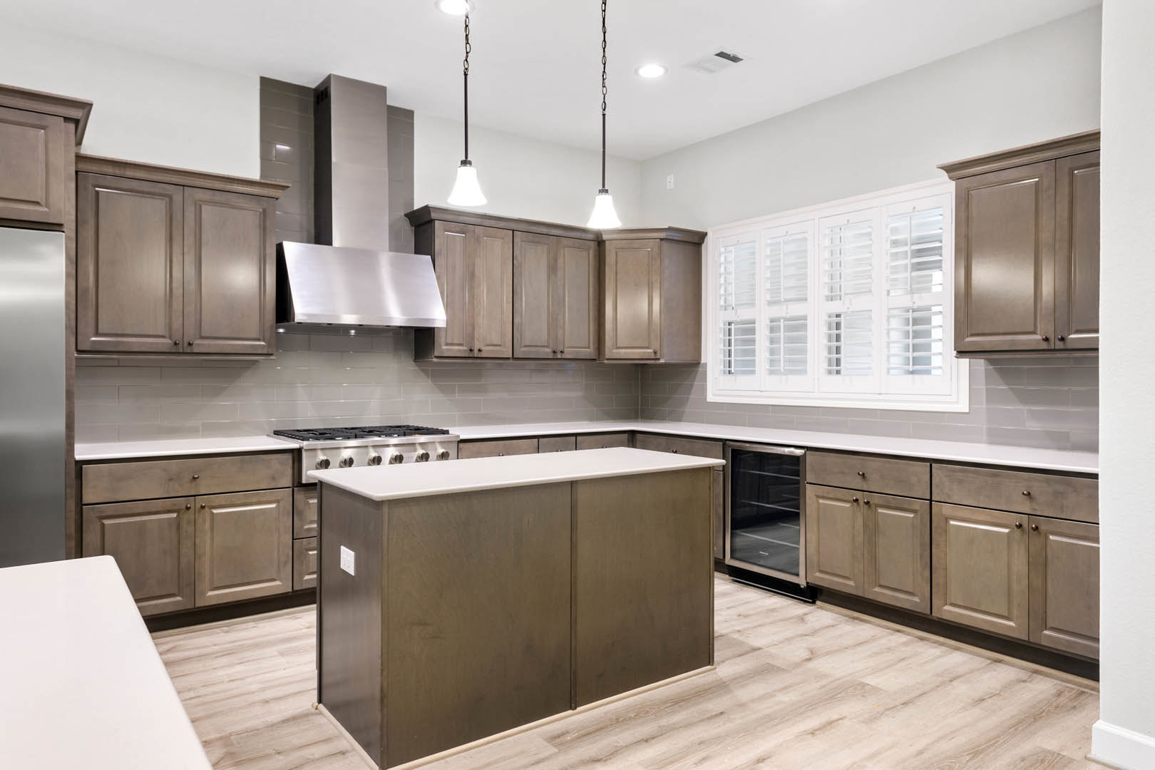 Open kitchen with white cabinetry, stainless steel stove, central island with quartz countertop, wood flooring, glass door reflecting shelving, and white walls with brown trim