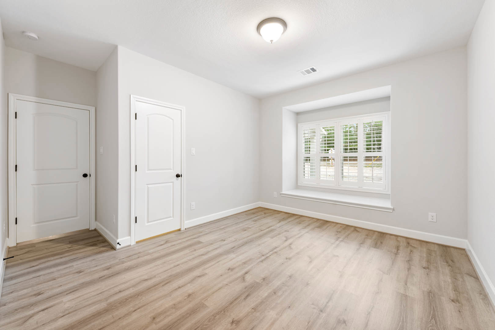 Wood flooring in a bright room with a white door featuring black knobs, window with blinds, plaster walls, and ceiling light fixture