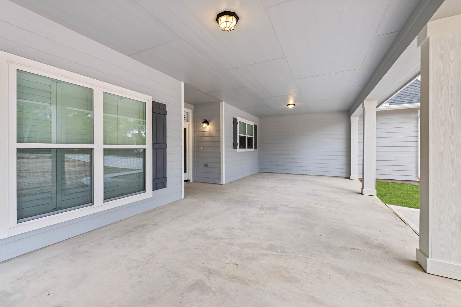 Two porches with white-trimmed windows, glass ceiling light fixture, concrete patio door, and green lawn in front of a custom home.