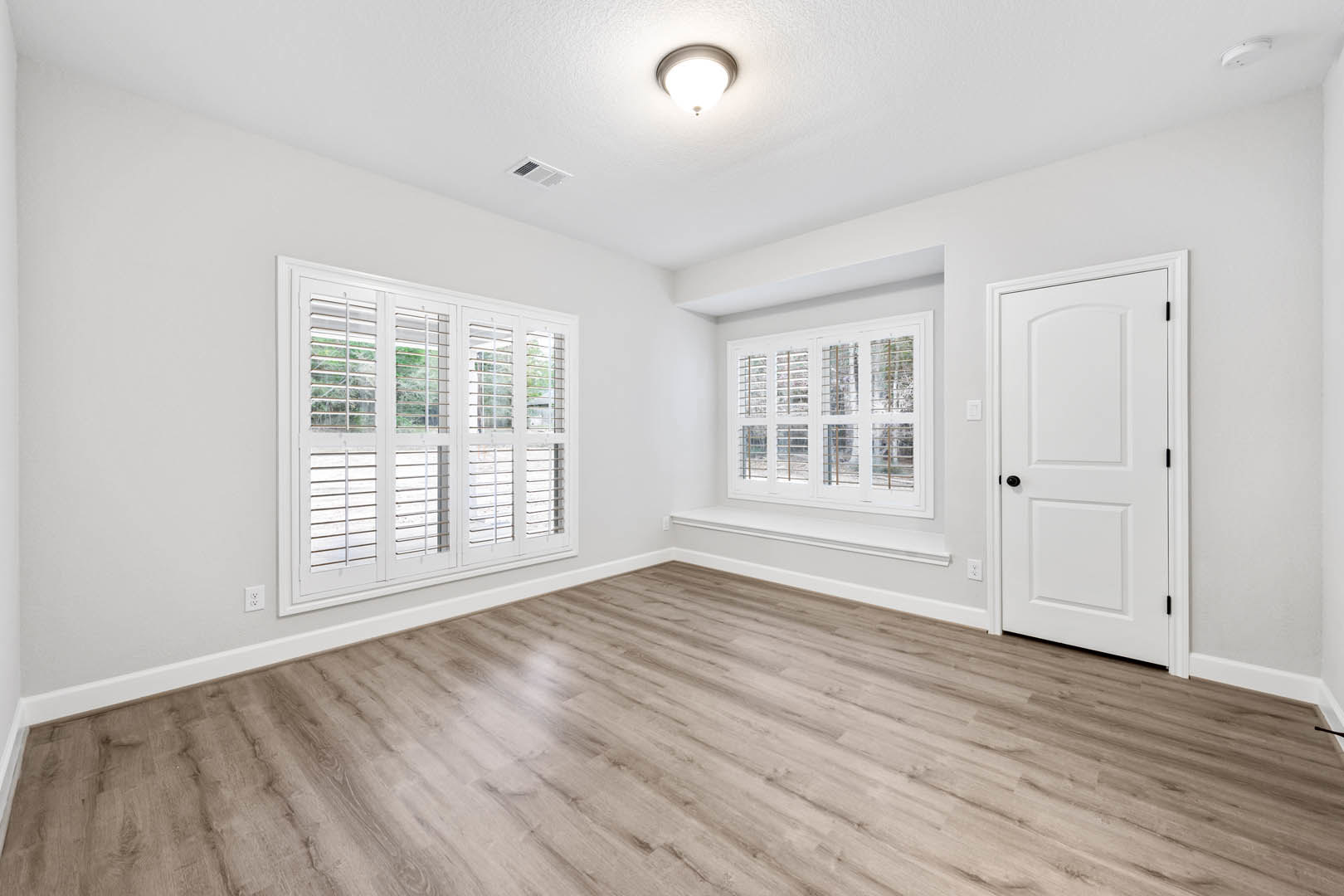 Wood floor room with white door featuring black knobs, white windows with blinds, and ceiling light fixture