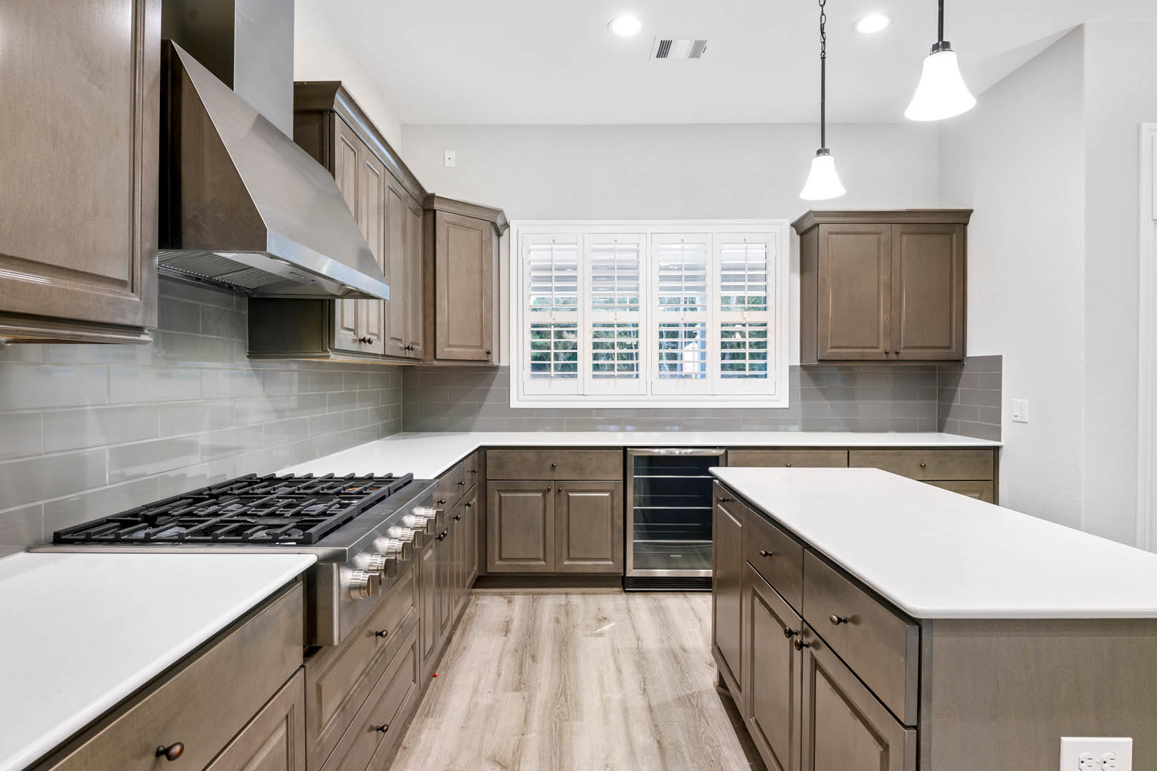 Modern kitchen with white cabinetry, stainless steel stove and oven, quartz countertops, tile backsplash, undermount sink, and stainless steel range hood