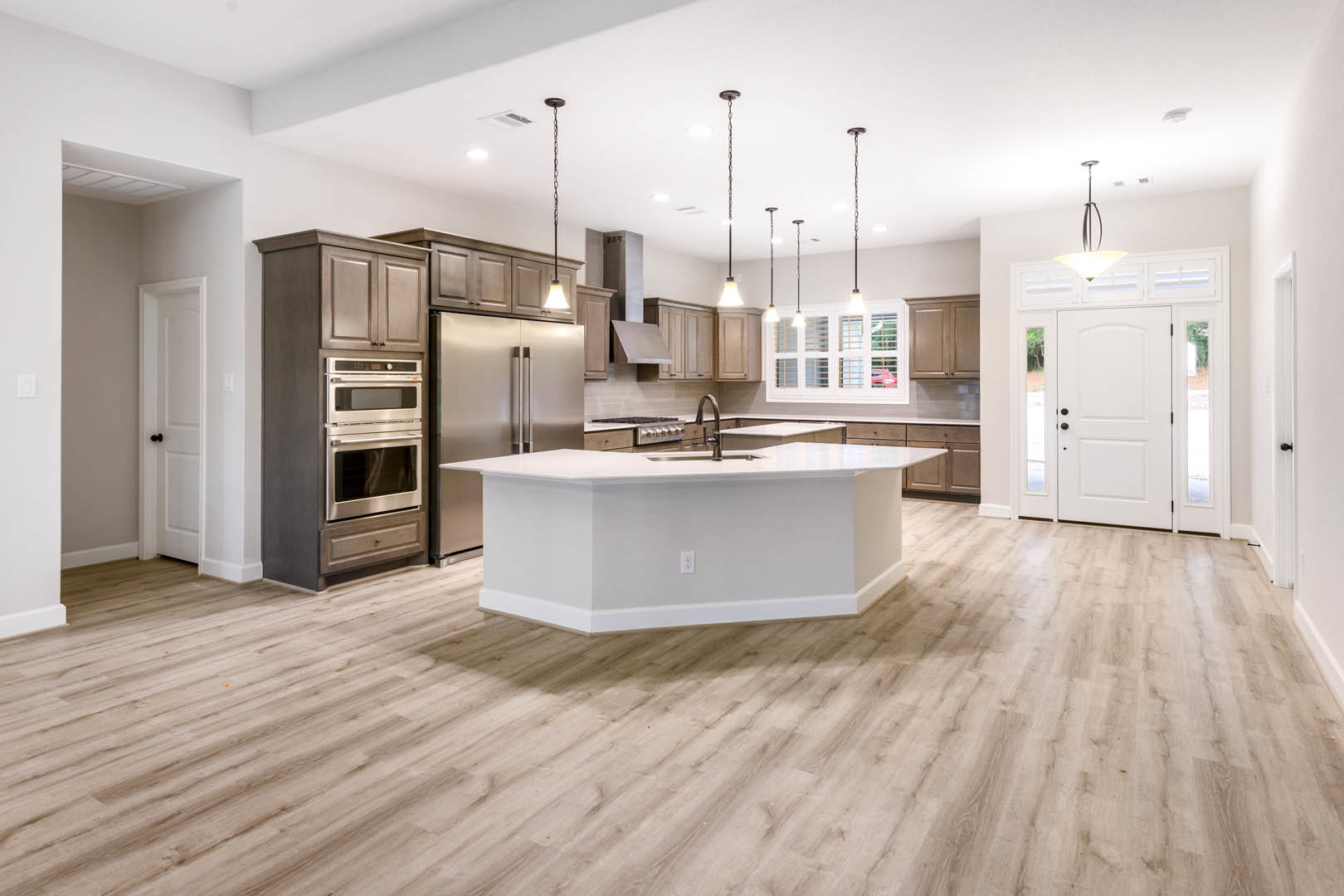 Kitchen with light wood flooring, white cabinetry, central white island featuring a built-in sink, stainless steel oven, white dining table, and glass-paneled door against white