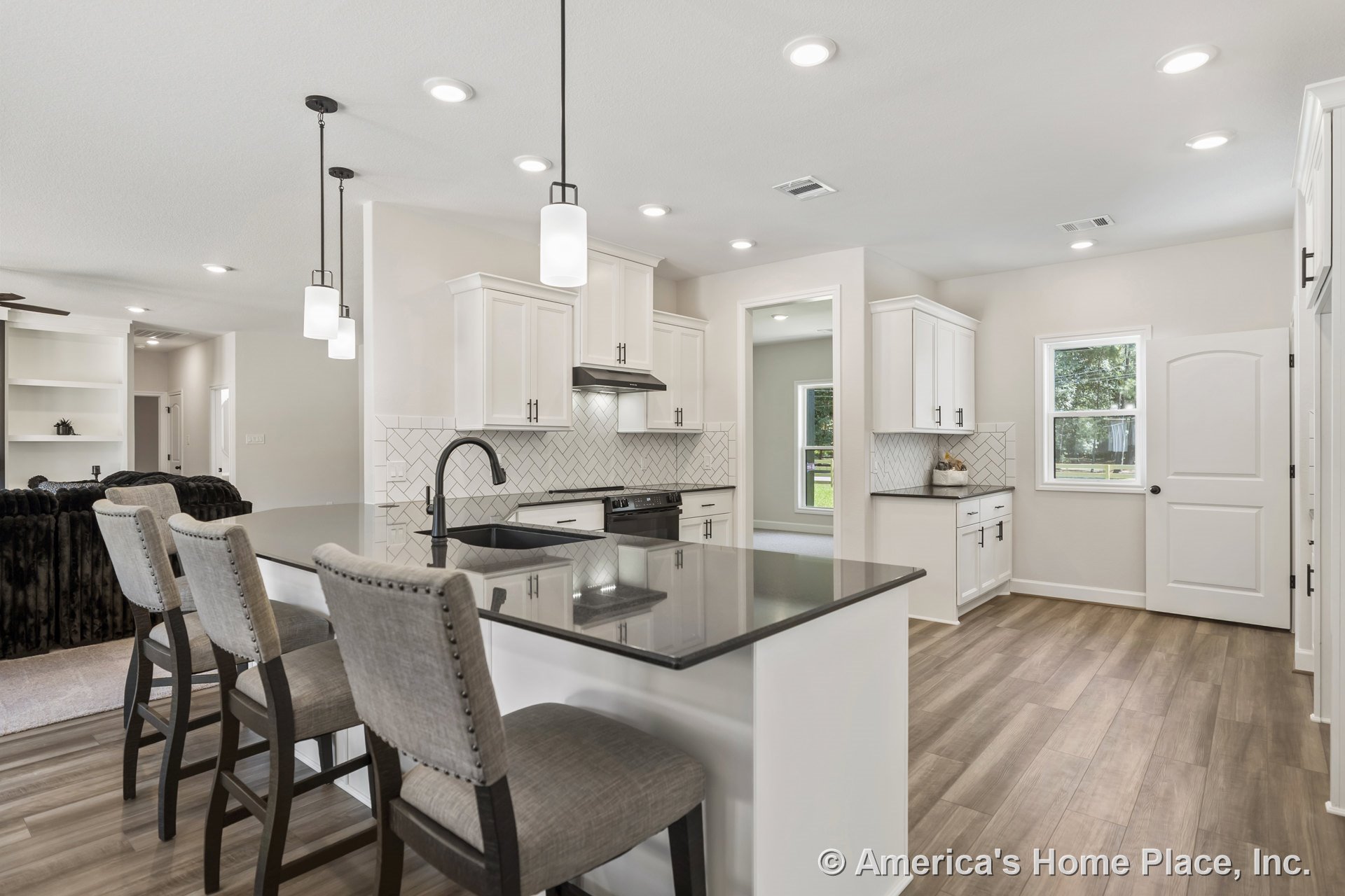 White shaker cabinetry and a black stone countertop island with integrated sink and faucet, herringbone tile backsplash, built-in stainless steel range hood, pendant and recessed