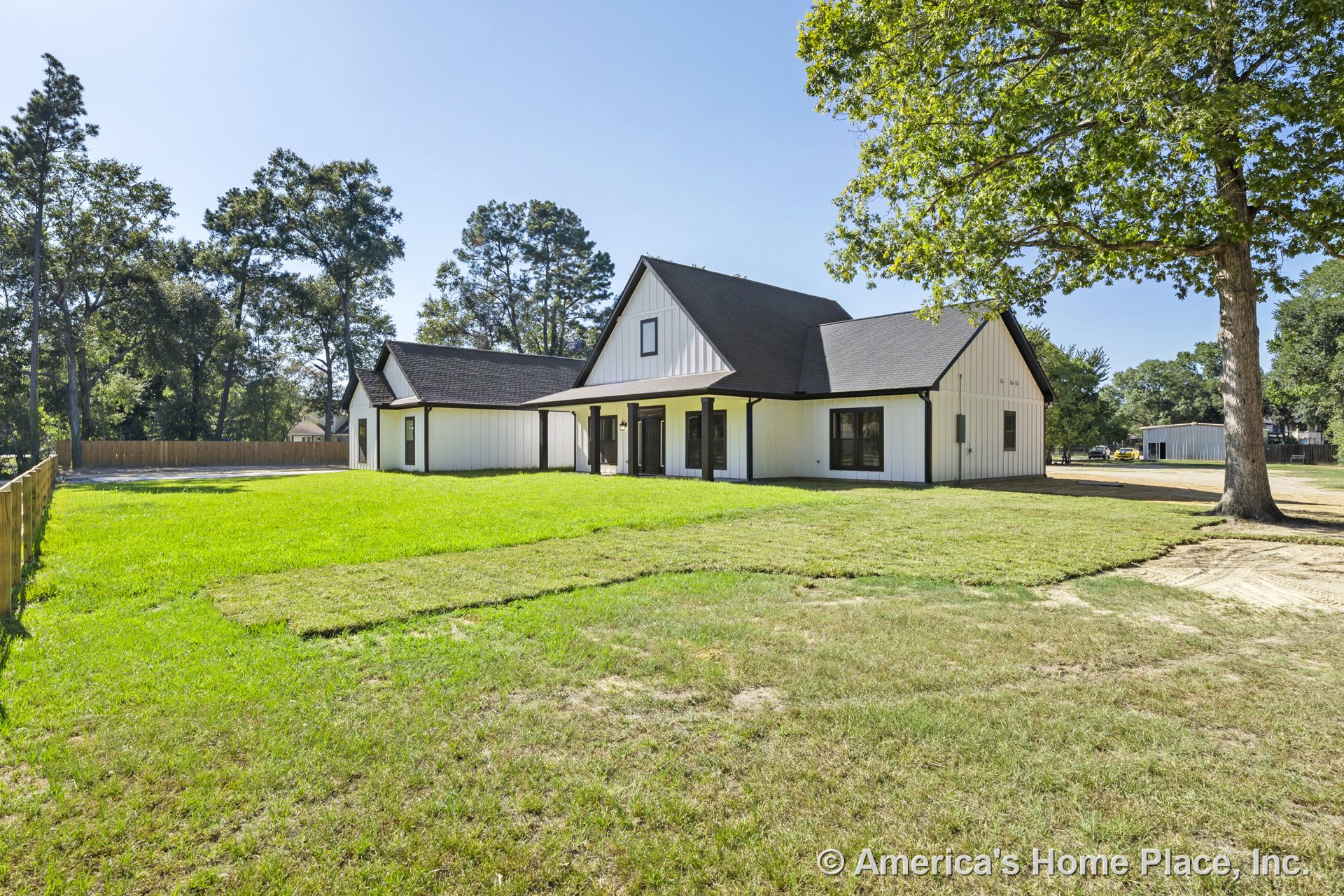 Modern farmhouse exterior with white board and batten siding, black trim and black framed windows, covered front porch, prominent gabled roof, attached garage, and expansive grassy