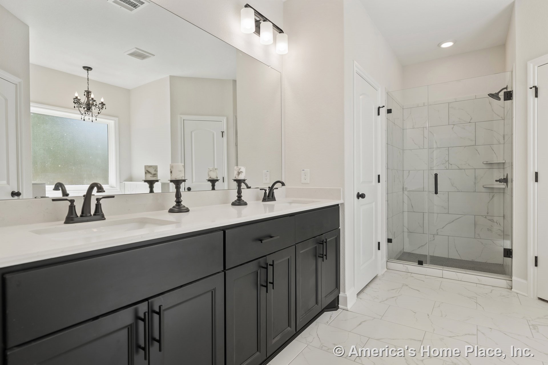 Double vanity with black shaker cabinets and quartz countertop, glass shower enclosure with large marble-look tile, expansive wall mirror, built-in lighting, chandelier, white