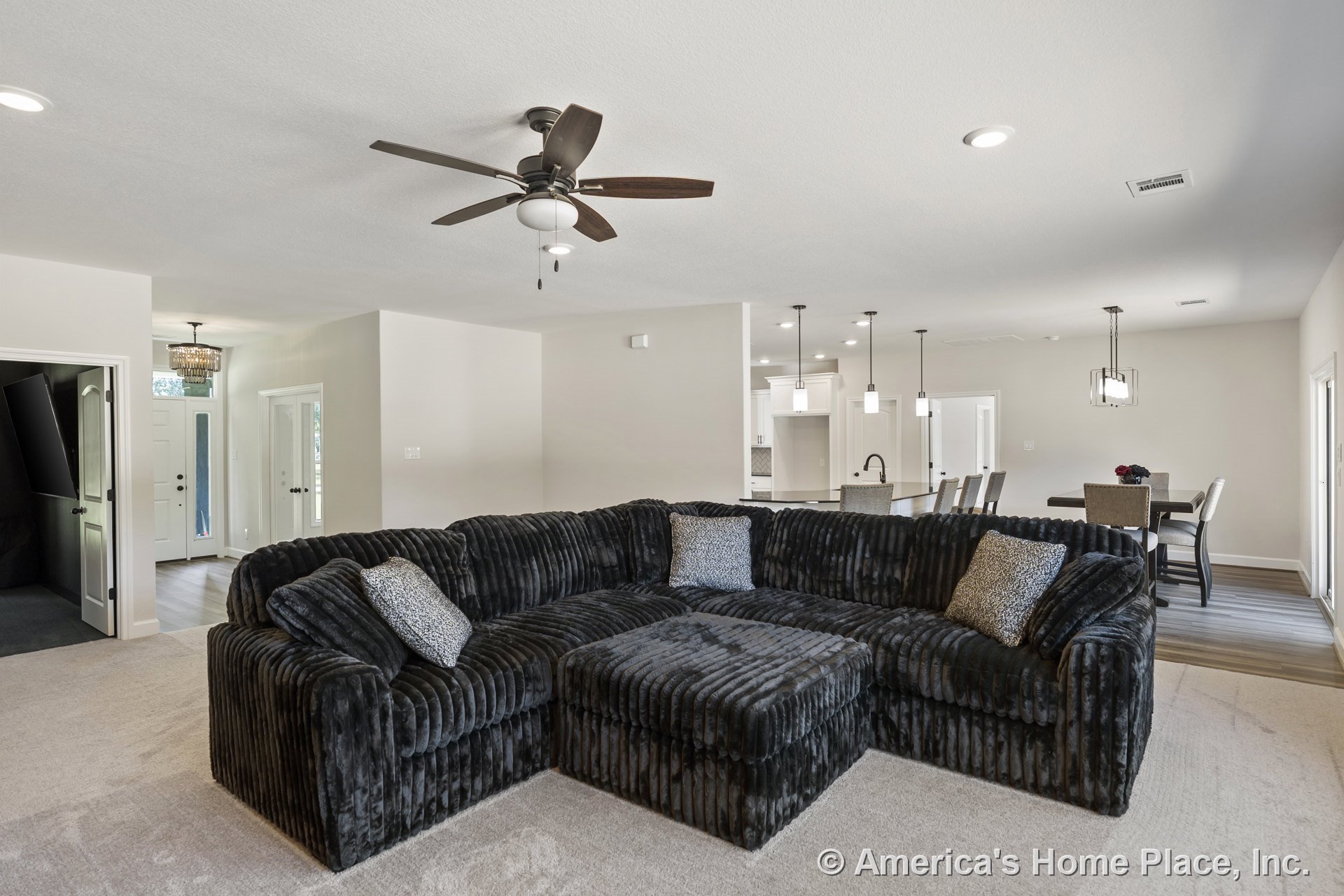 Open floor plan with recessed ceiling lights and dark ceiling fan in the living area, carpeted flooring transitioning to wood-look floors in the dining area, kitchen with white