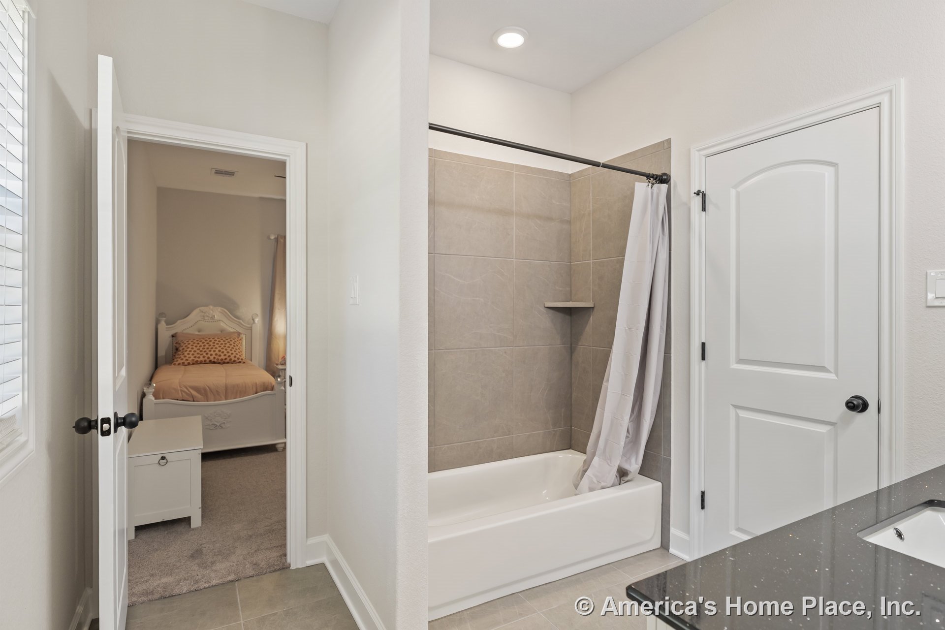 Tiled tub-shower combo with built-in shower shelf, black granite vanity countertop, ceramic floor tile, recessed ceiling light, white paneled interior doors, and neutral wall