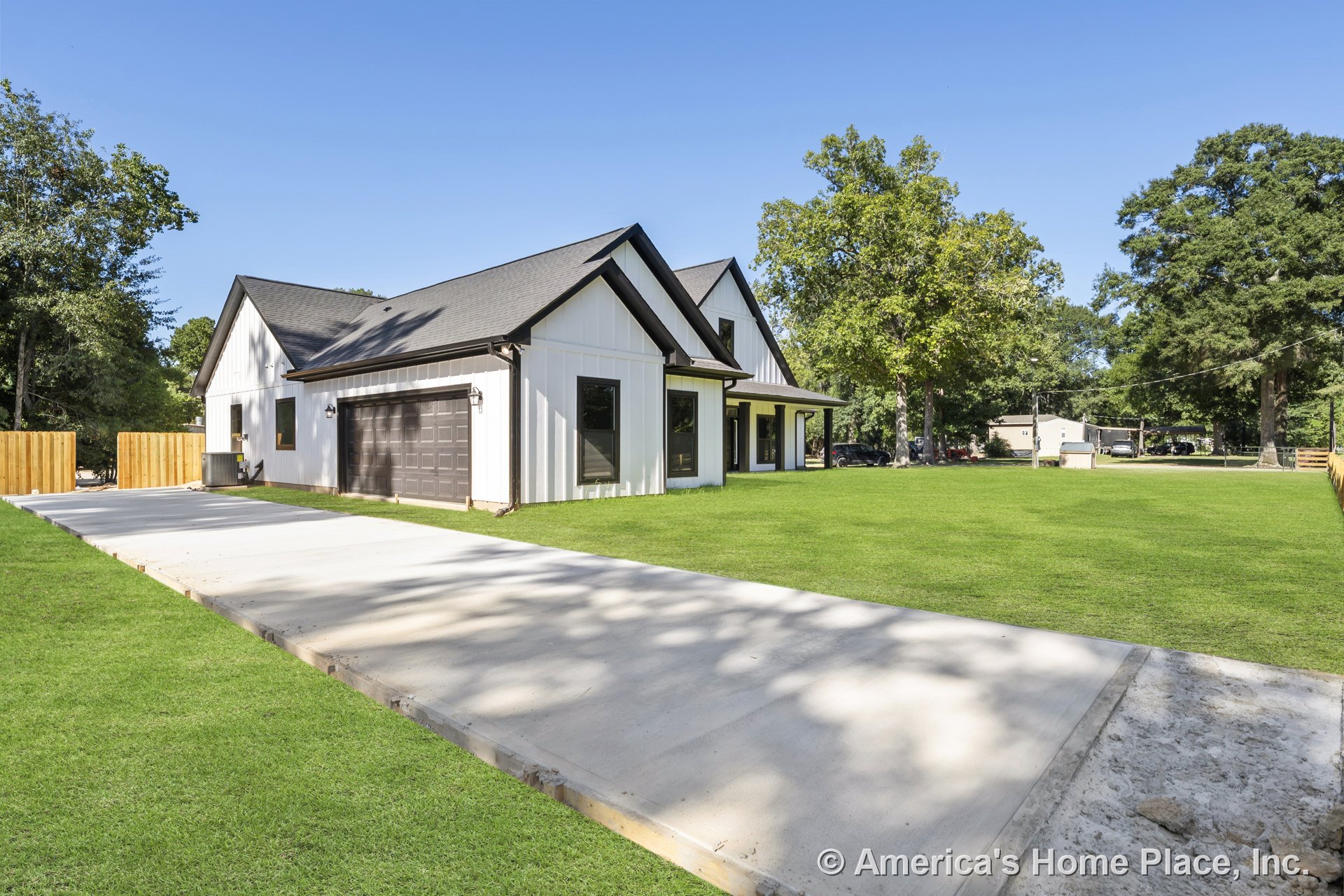 Modern exterior with board and batten siding, black trim, black framed windows, gabled roof, covered front porch, attached two-car garage, and concrete driveway.