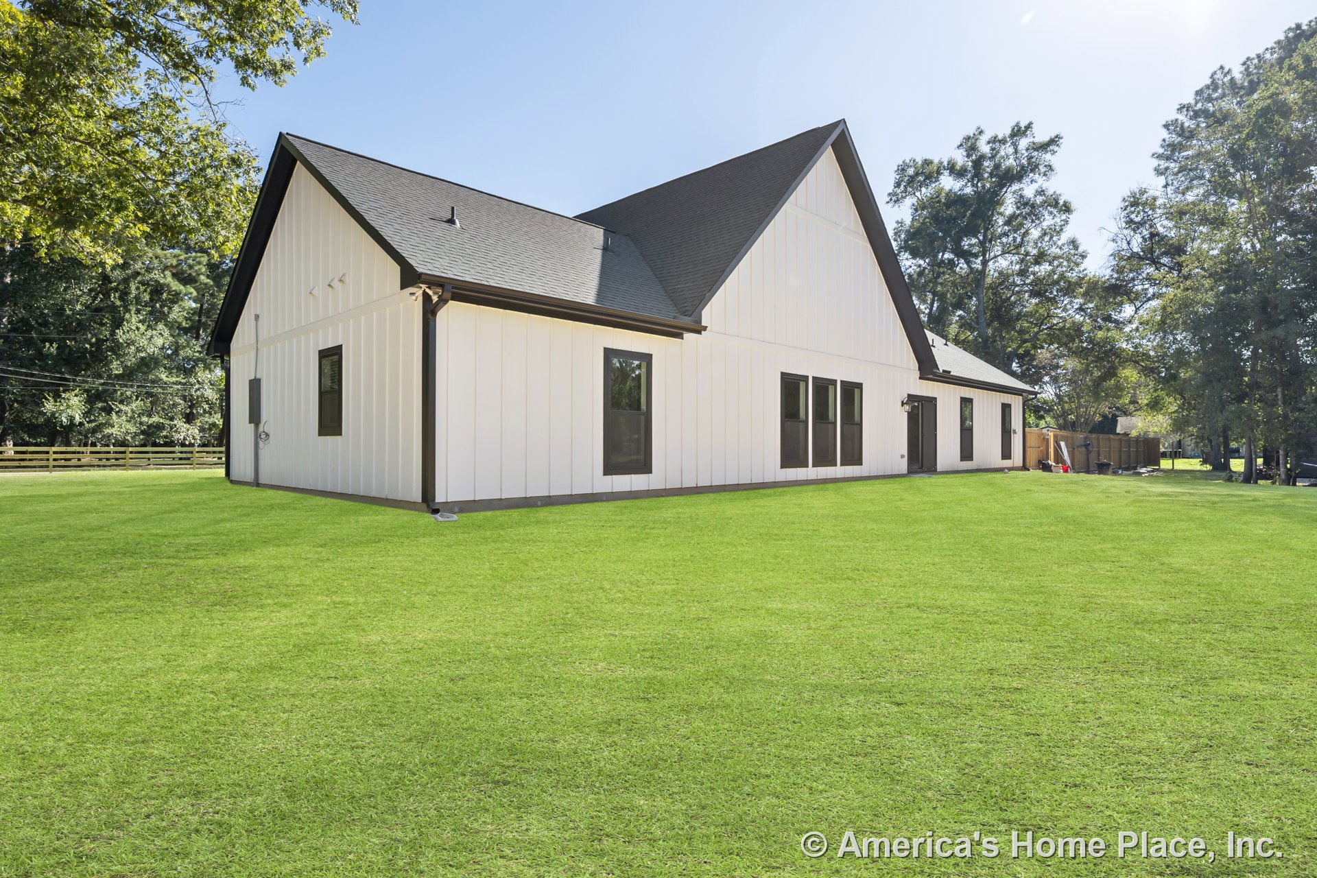 White vertical board and batten siding with contrasting dark window trim, multiple gabled rooflines with black shingles, large windows, and a spacious green lawn.