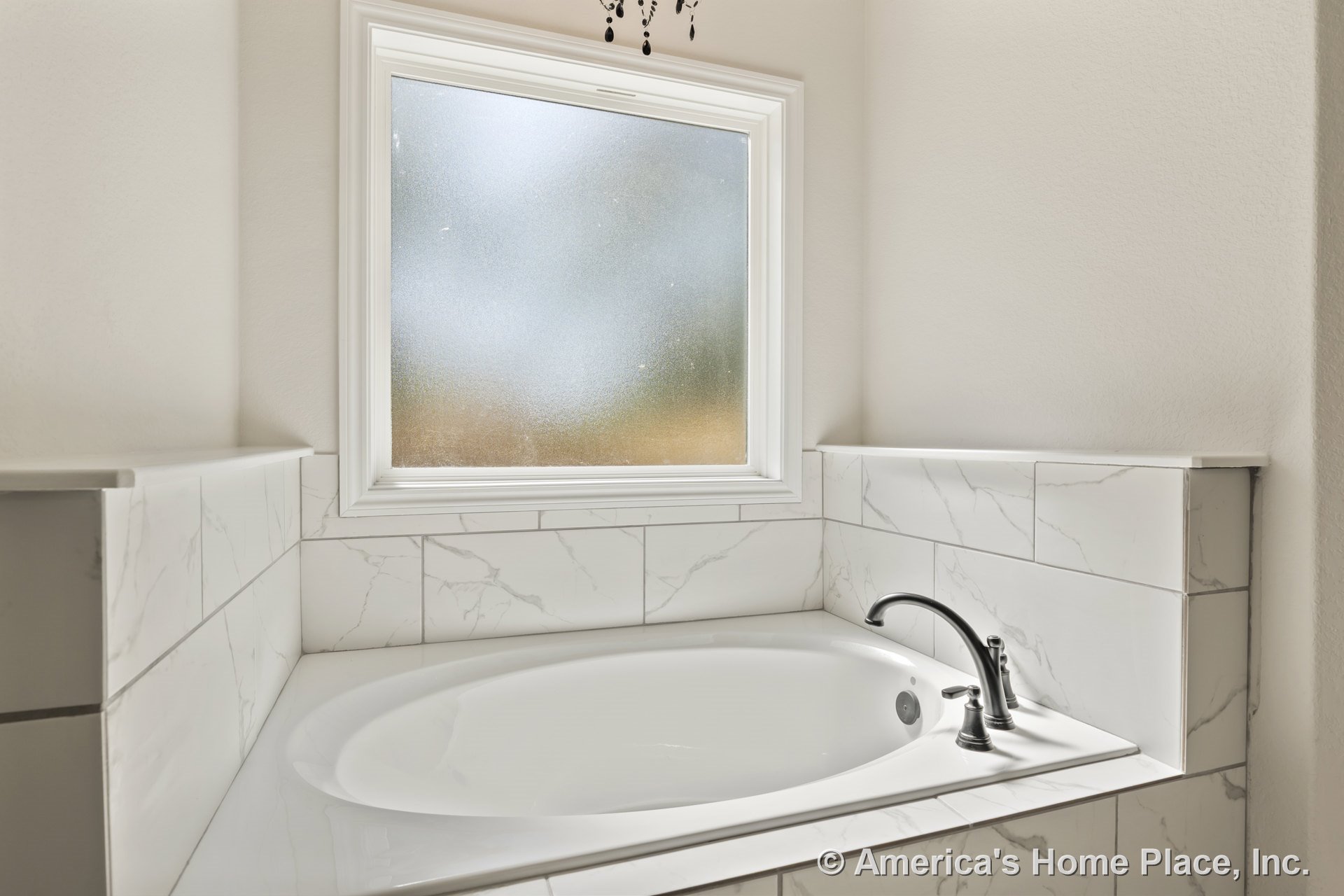 Oval soaking tub with marble-look tile surround beneath a frosted window, chrome faucet fixtures, white trim, and neutral wall color.