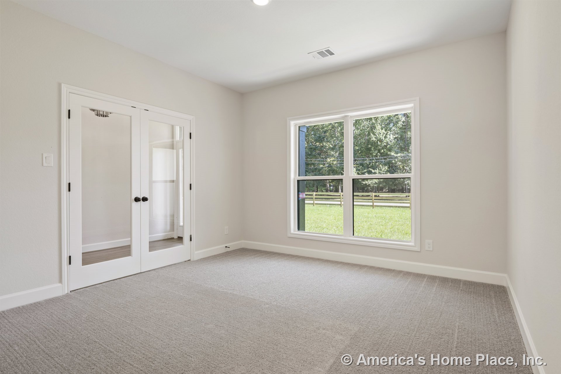 Carpeted room with double glass French doors, large window framed in white trim, white baseboards, smooth light-colored walls, and recessed ceiling light.