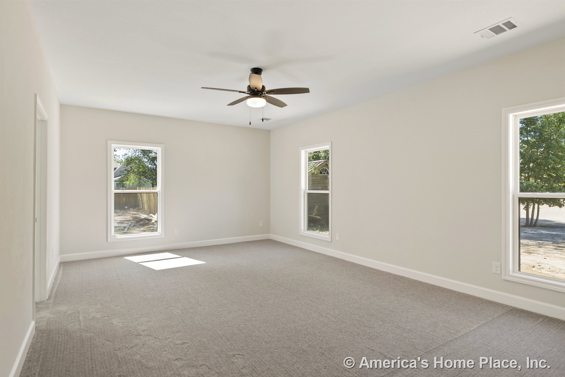 Spacious bedroom with neutral carpet flooring, three large windows allowing natural light, ceiling fan with integrated light fixture, smooth white ceiling, light beige walls, and
