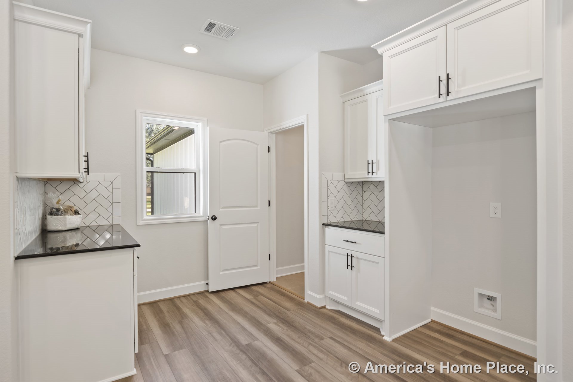 White upper and lower cabinets with black solid surface countertops, herringbone tile backsplash, wood-look vinyl plank flooring, recessed ceiling lights, laundry appliance