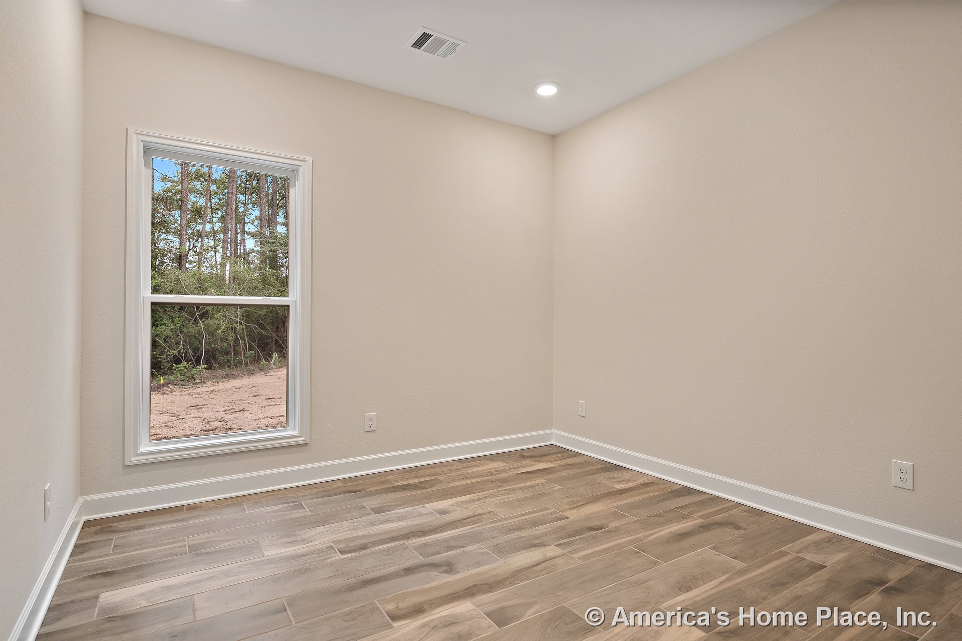 Small room with wood-look tile flooring, large window framed in white trim, white baseboards, recessed ceiling light, ceiling vent, and neutral painted walls.