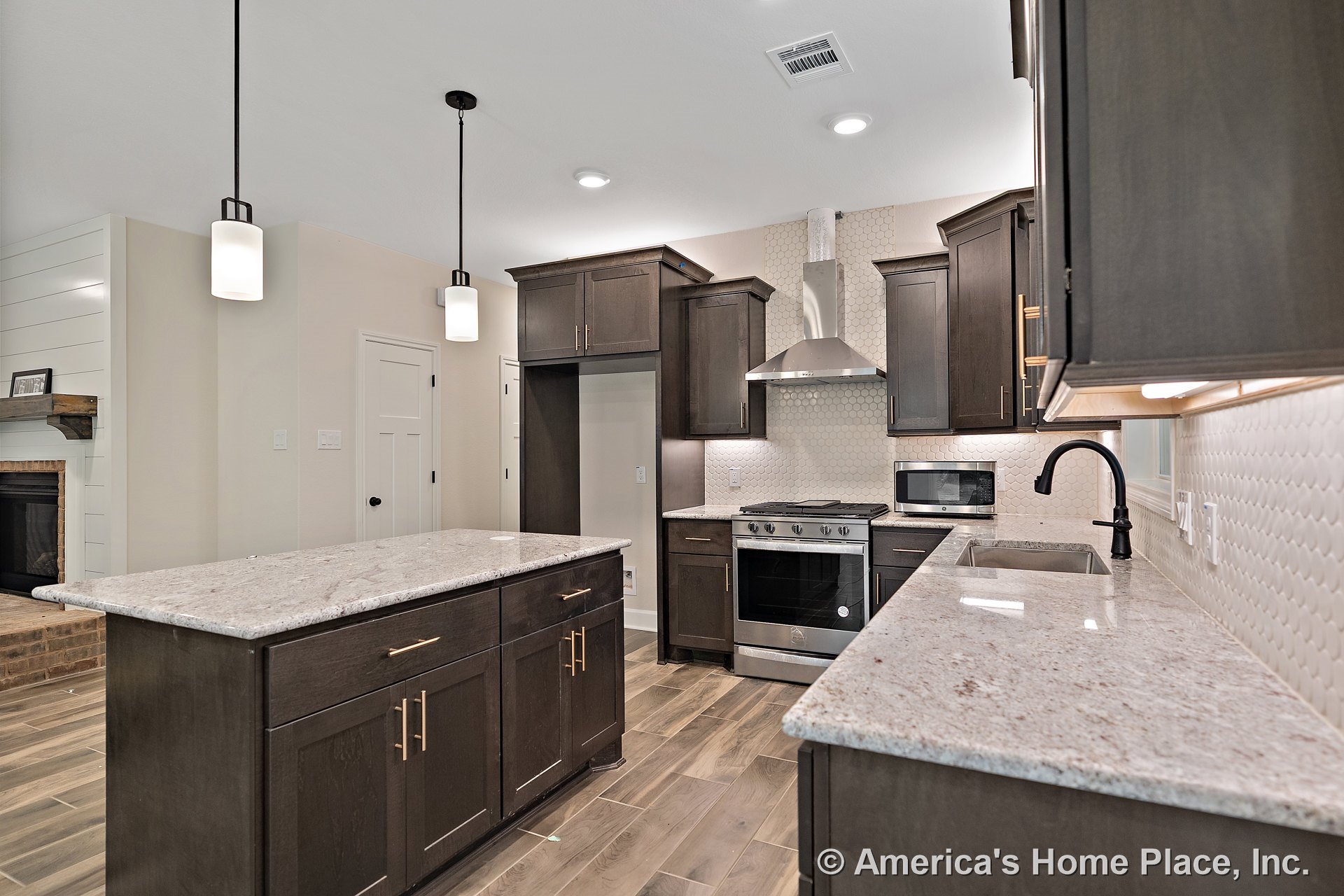 Dark wood cabinetry and built-in storage frame a kitchen with granite countertops, hexagonal tile backsplash, stainless steel range hood, pendant lighting fixtures, and a central