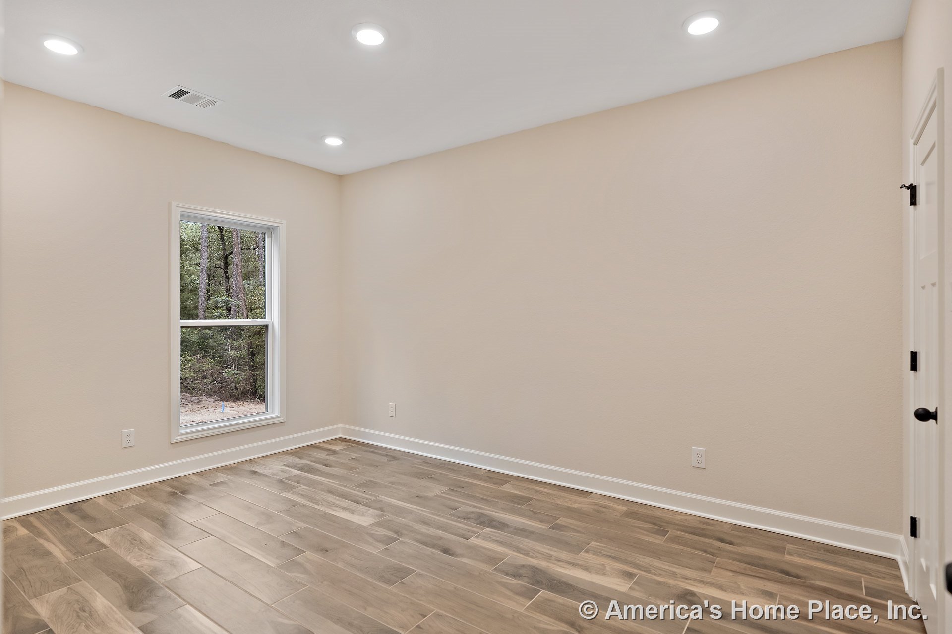 Bedroom with wood-look tile flooring, recessed ceiling lights, large single window framed in white trim, white baseboards, neutral wall color, and paneled door featuring black