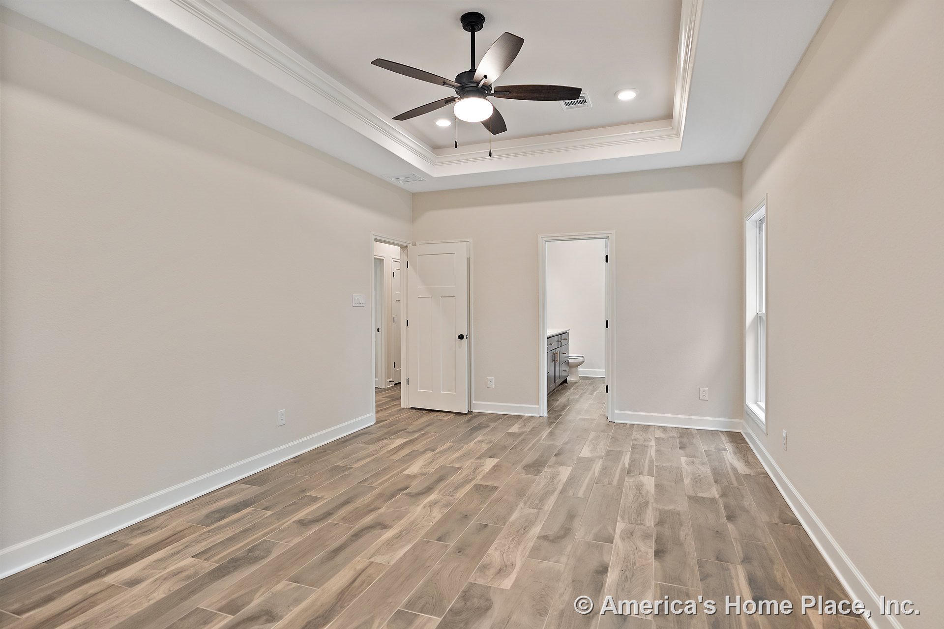 Wood-look tile flooring, tray ceiling with recessed lighting and ceiling fan, white trim and baseboards, bathroom entry with built-in cabinetry, interior door, large window