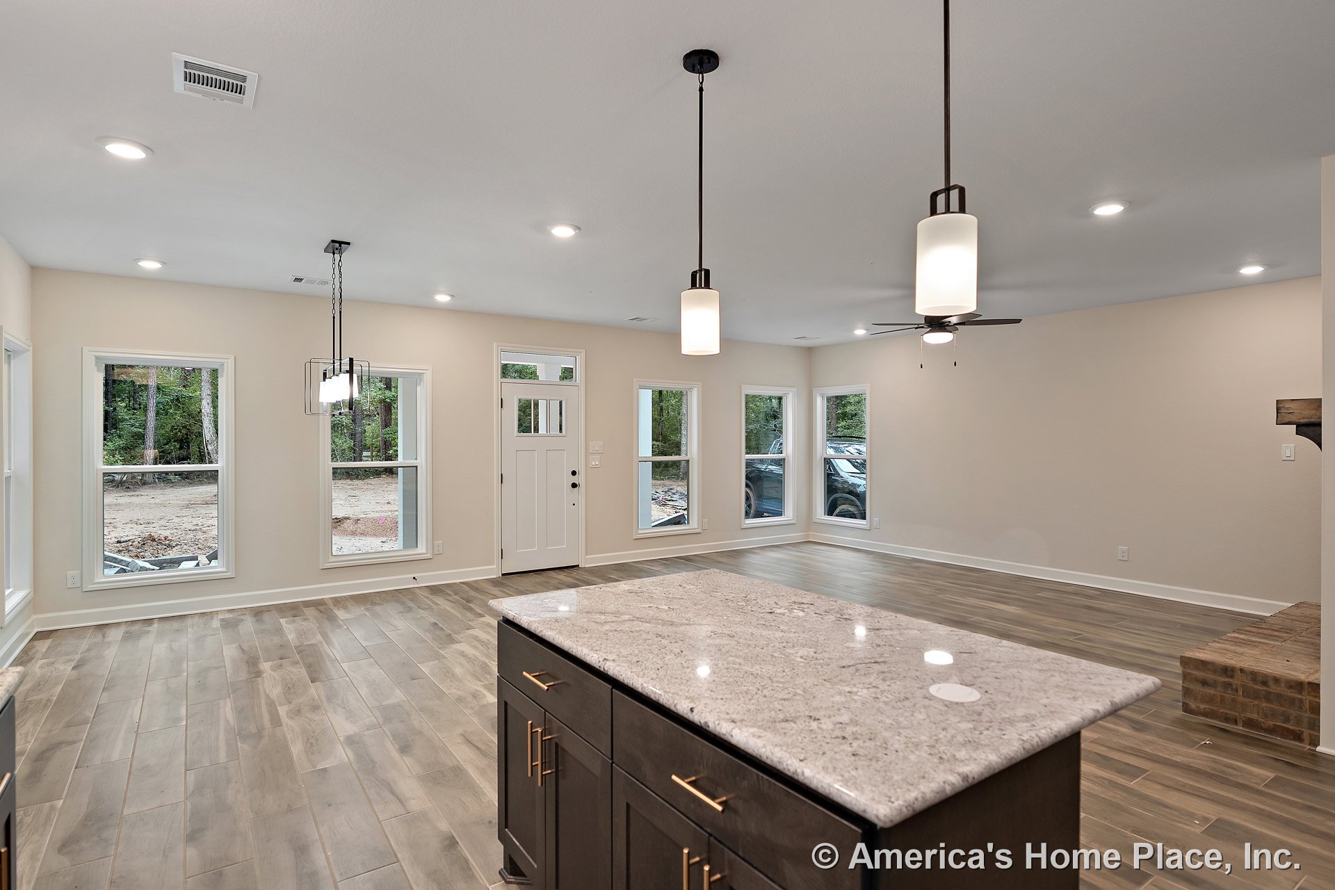 Open floor plan living area with wood-look tile flooring, kitchen island featuring a stone countertop and dark cabinetry with gold hardware, pendant and recessed ceiling lights