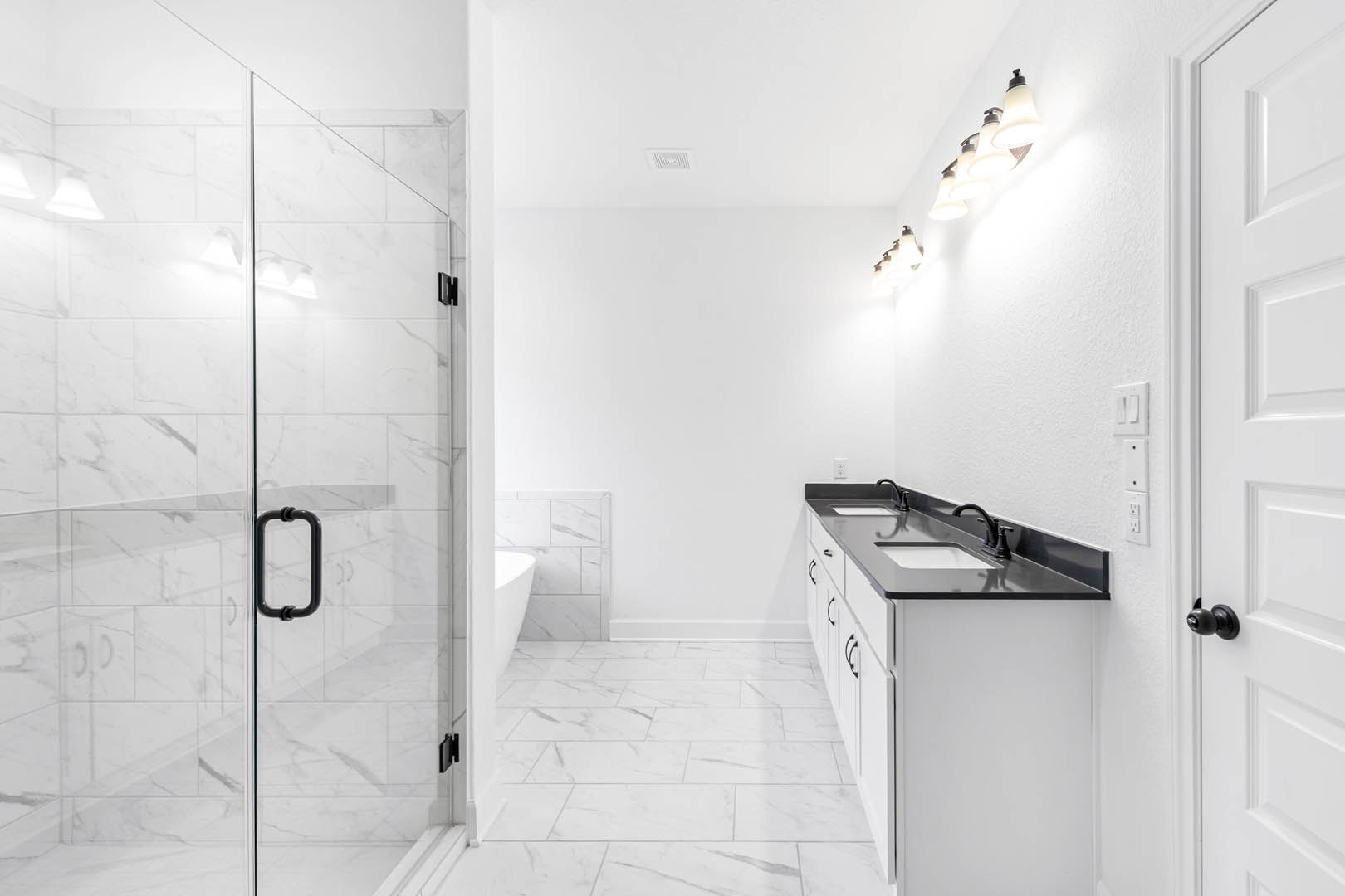 Bathroom with marble tile floor, white walls, glass shower door with black handle, black sink, and row of wall-mounted lights