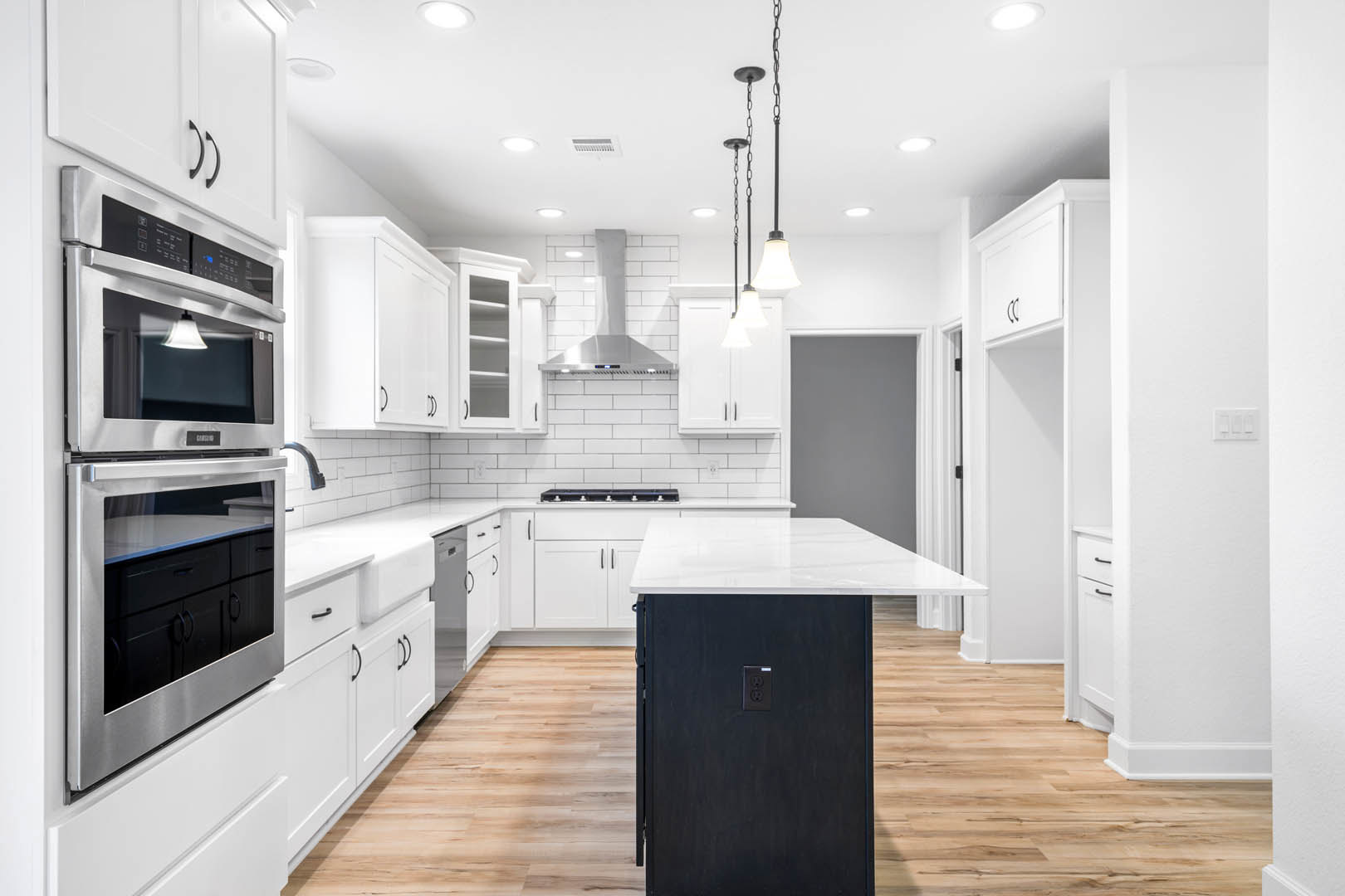White shaker cabinets and black kitchen island with quartz countertop, stainless steel microwave with glass door, pendant light with white shade, white wall switch, light hardwood