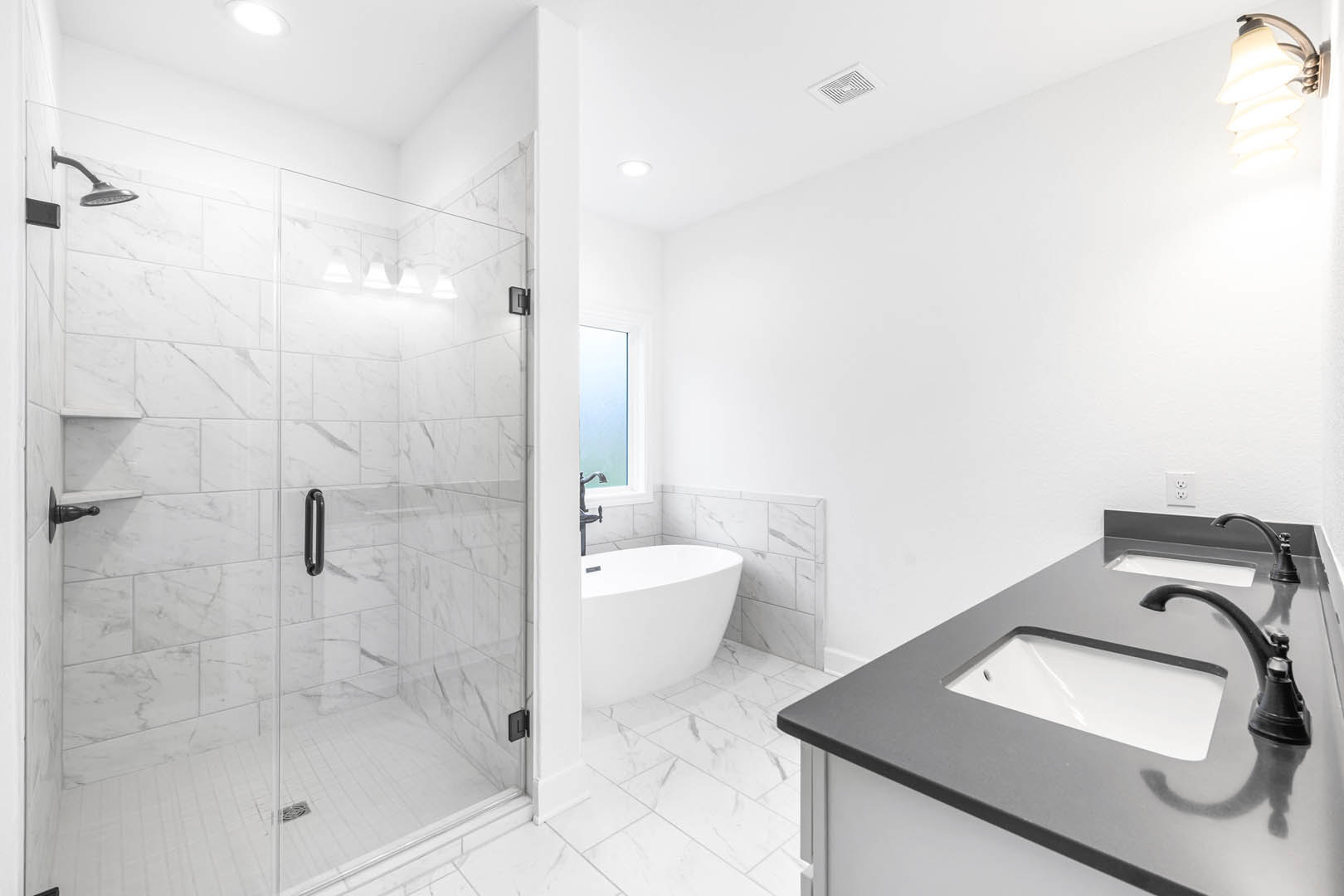 Bathroom featuring glass-enclosed shower with chrome shower head, freestanding white bathtub, wall-mounted sink with modern faucet, tile flooring, and contemporary light fixture