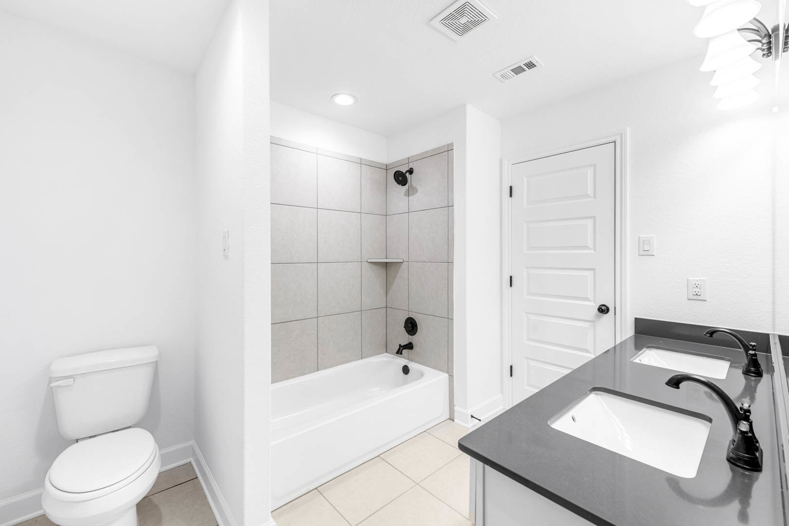 White freestanding bathtub with matte black fixtures, modern rectangular sink with chrome faucet, light gray tile walls, and contemporary wall-mounted lamp in a spacious bathroom.