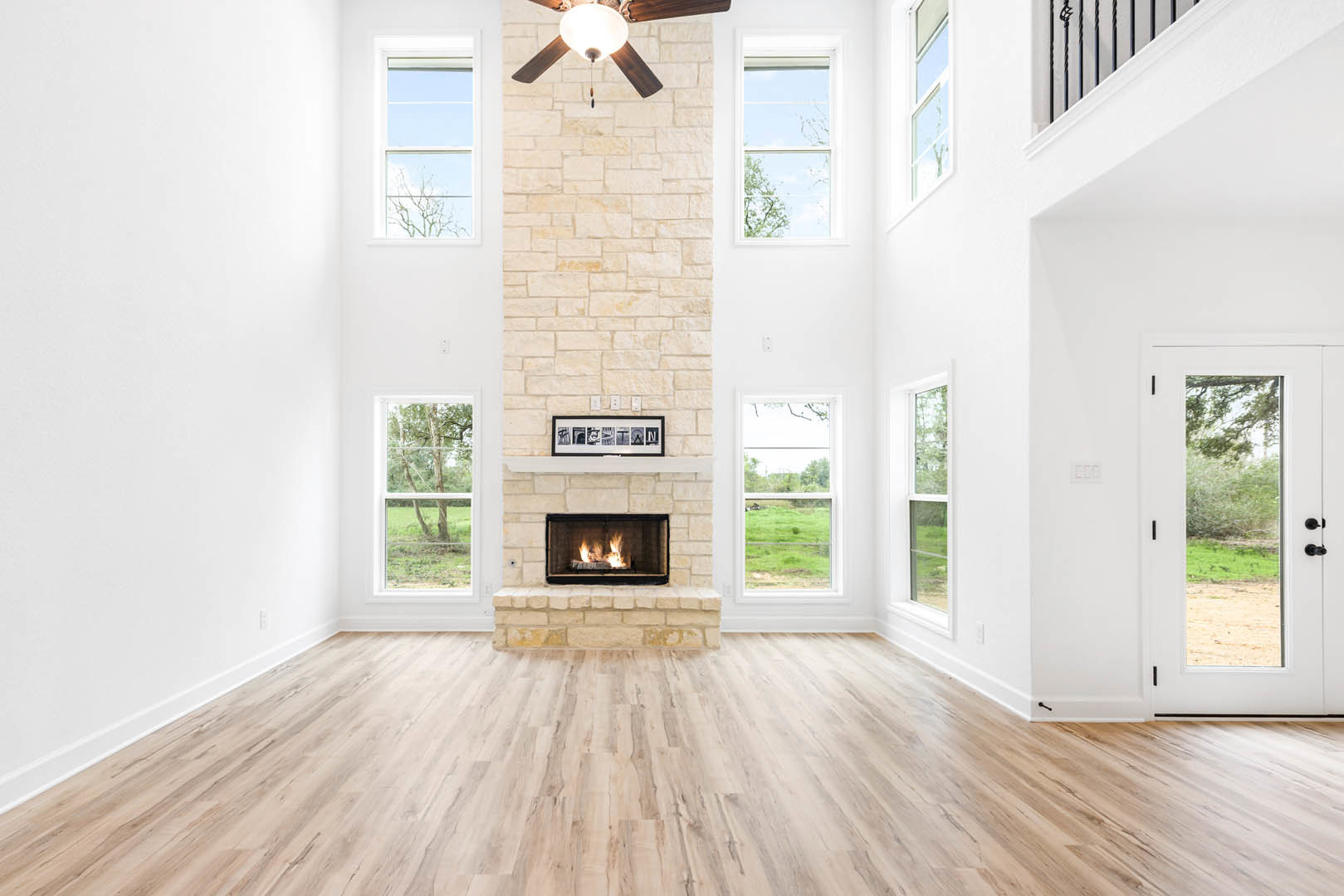 Living room with hardwood floors, brick fireplace with active fire, ceiling fan with light, and framed pictures arranged on the wall.
