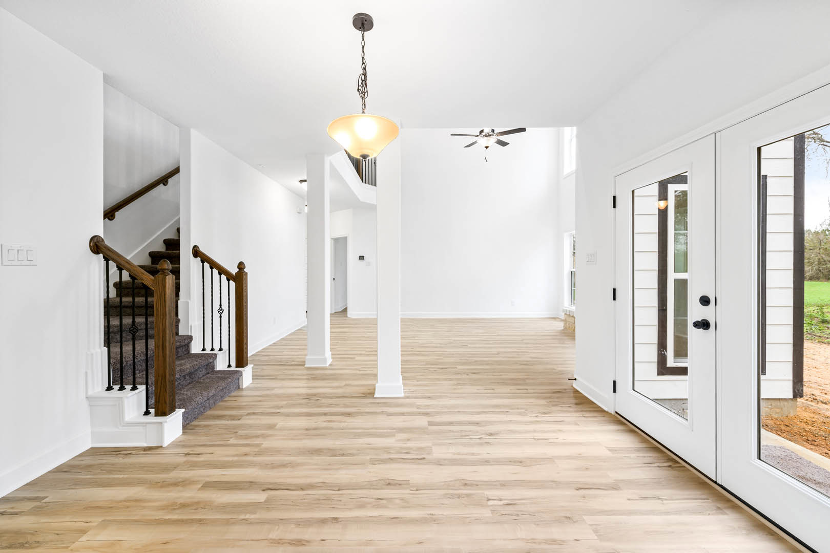 Hallway with wood flooring, white pillars, staircase featuring black railing, and ceiling fan with integrated light fixture