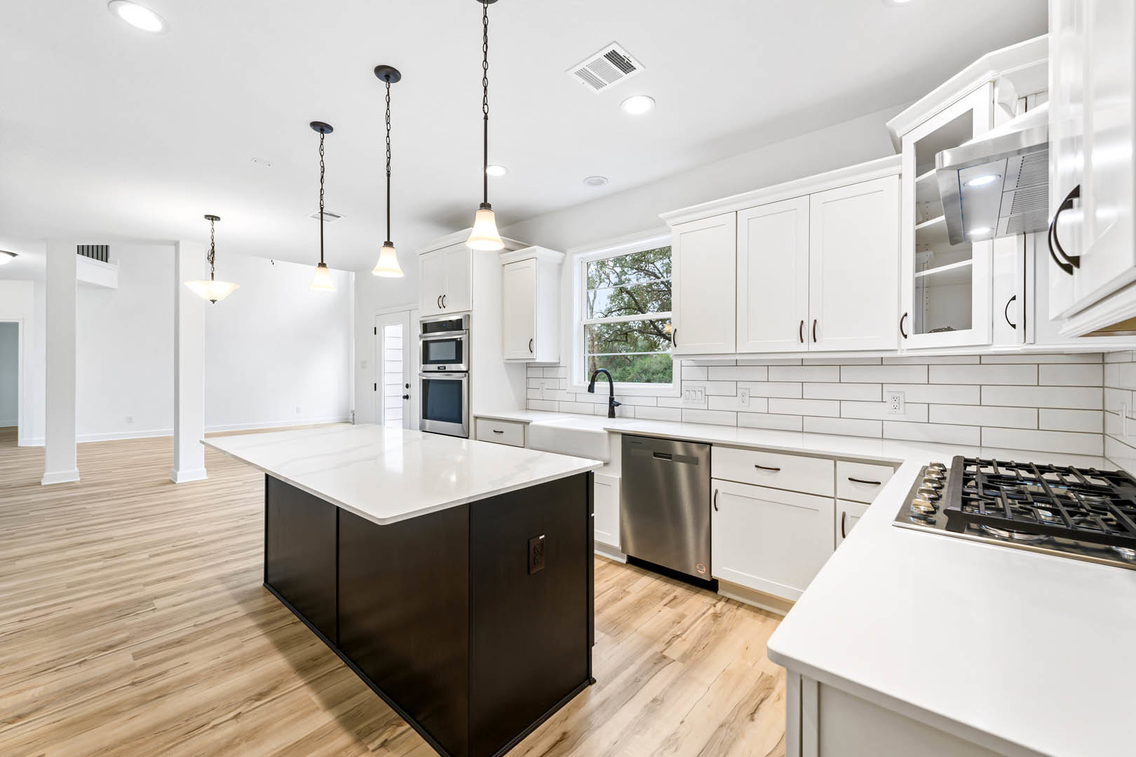 Kitchen with white cabinetry, white countertops, central island, stainless steel microwave and dishwasher, black metal grate, black stovetop, tile backsplash, and wood flooring