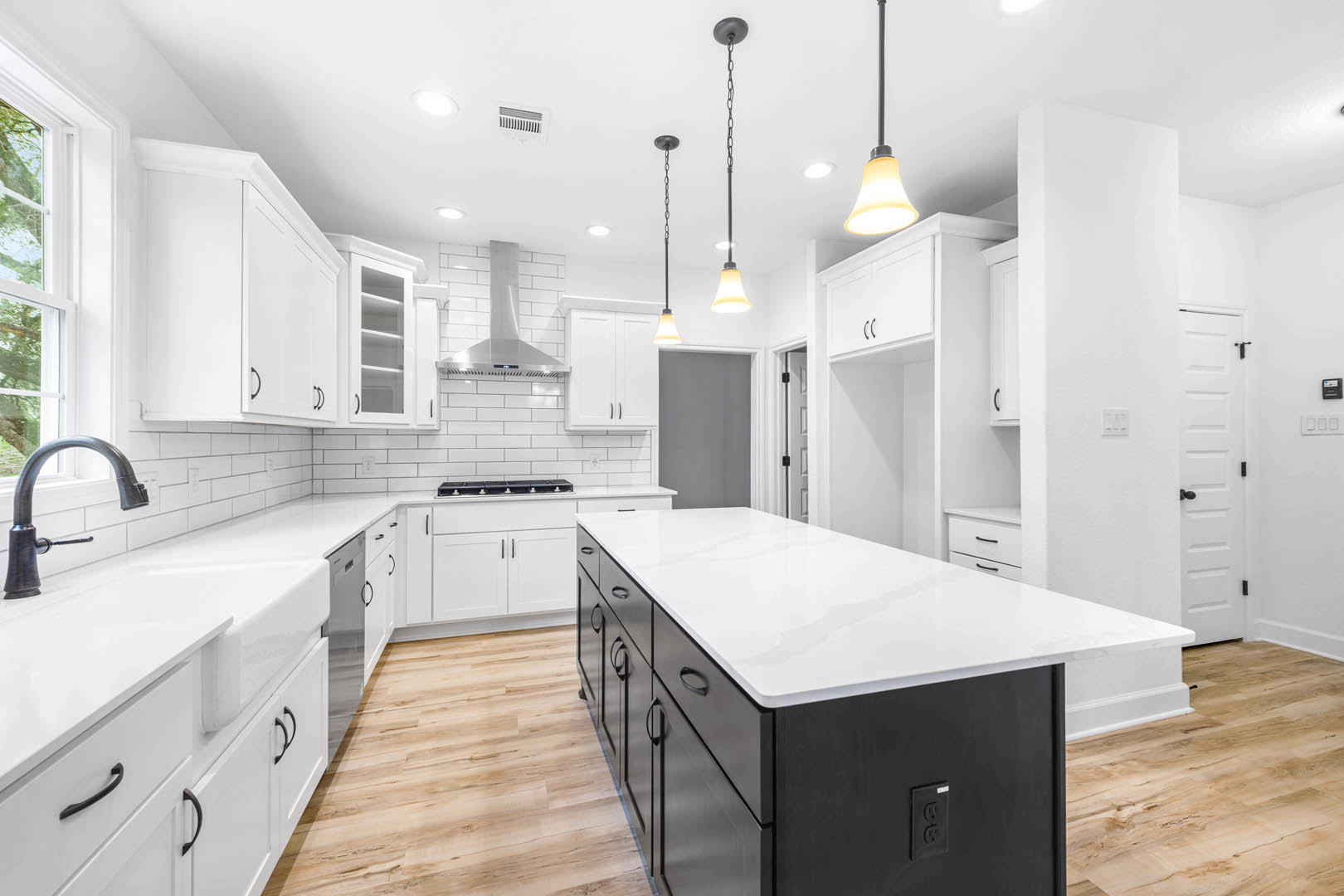 White kitchen with shaker cabinets, quartz countertop, stainless steel sink and faucet, tile backsplash, pendant light fixture, and visible power outlet on the wall.