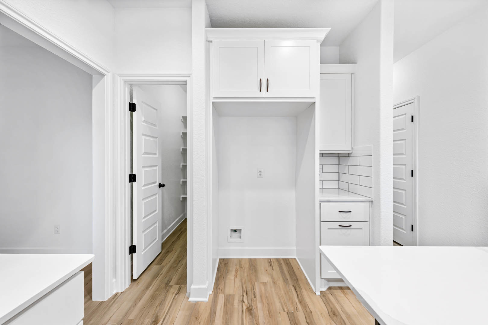 White kitchen with flat-panel white cabinets, light wood flooring, white quartz countertop, and a white door with black hardware