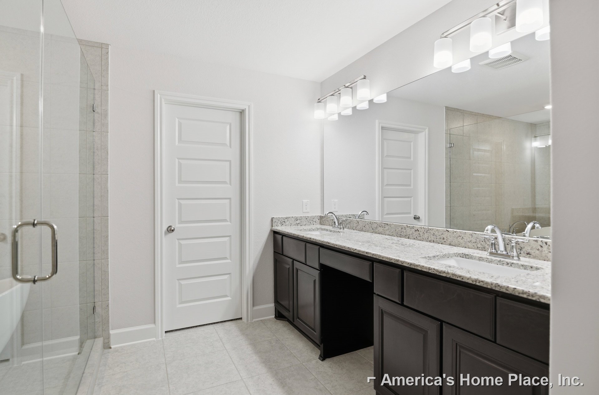 Bathroom with double sink vanity, white cabinetry, stone countertop, chrome faucets, white door with silver knob, tiled floor and walls