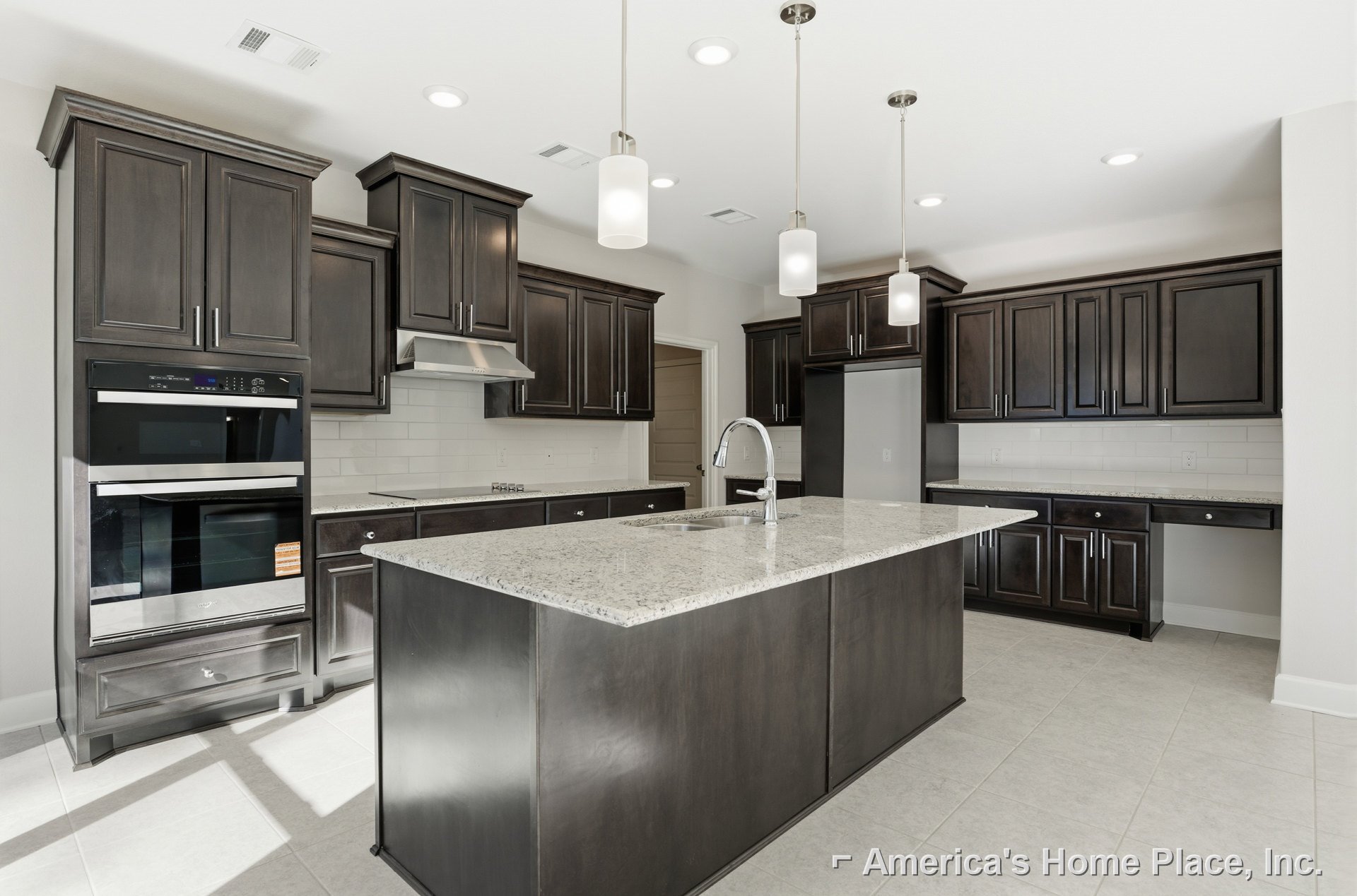 Spacious kitchen featuring a large central island with built-in sink, stainless steel oven with glass door, white overhead light fixture, and modern cabinetry.