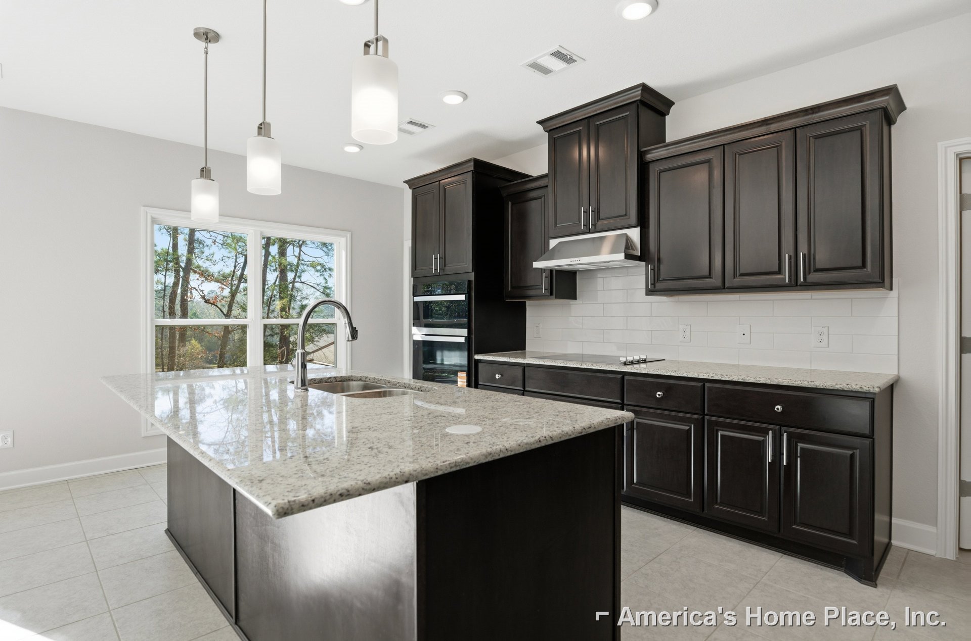 Spacious kitchen featuring a granite island with built-in sink, white cabinetry, stainless steel appliances, pendant lights, and a red light fixture on a pole.
