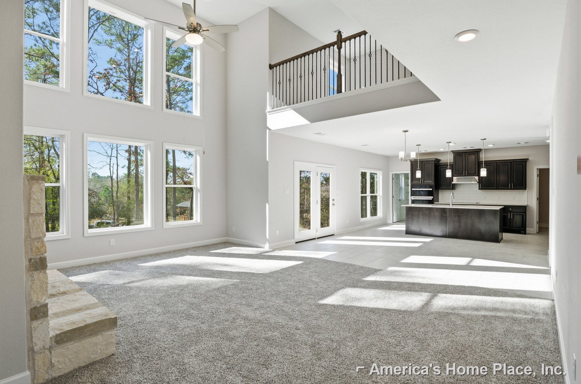Spacious white open-plan room featuring a modern kitchen with stone backsplash, countertop sink, carpeted area, staircase, large window overlooking trees, and white door with glass