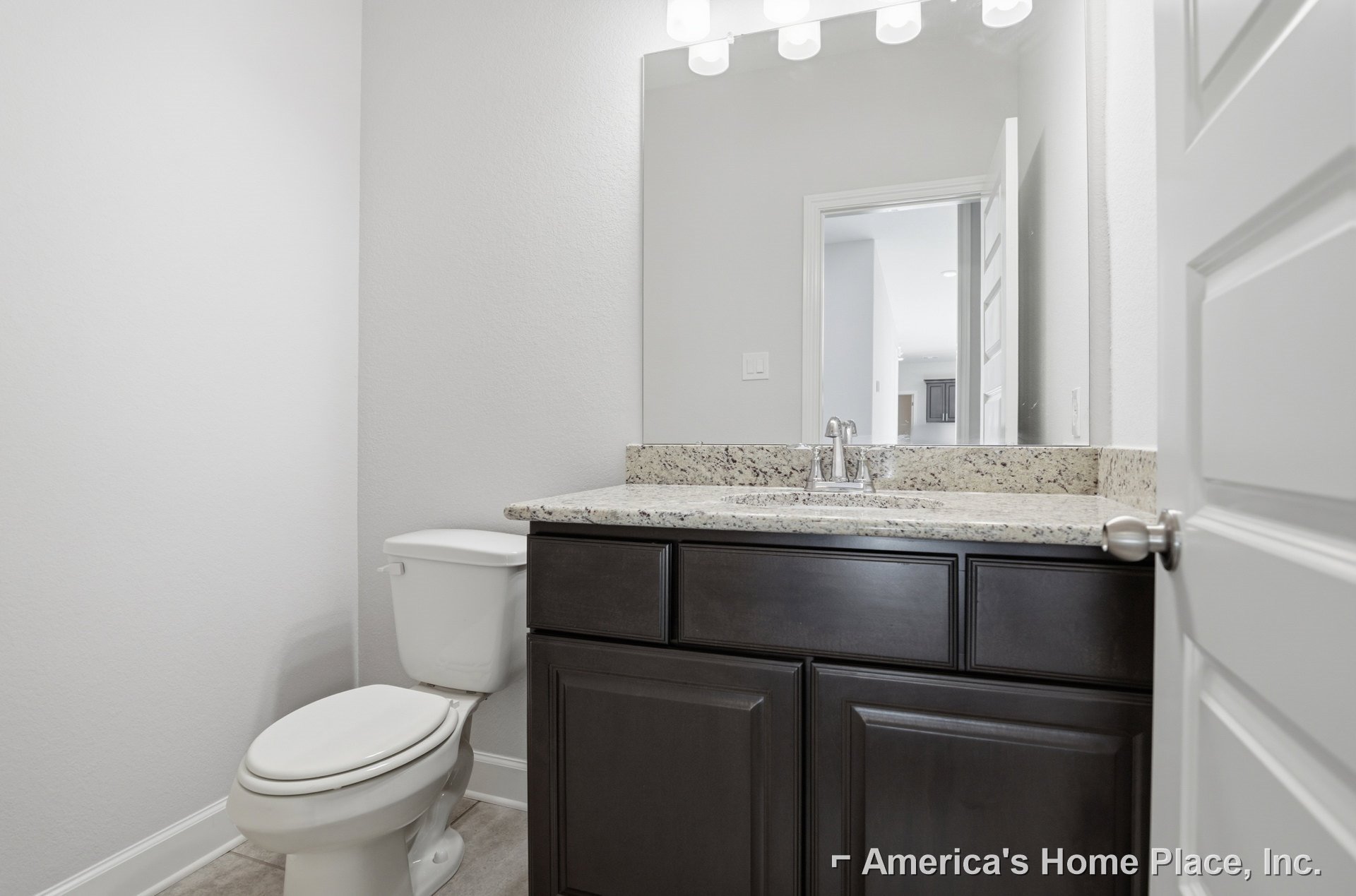Bathroom with marble countertop, undermount sink, chrome faucet, and white toilet against tiled wall