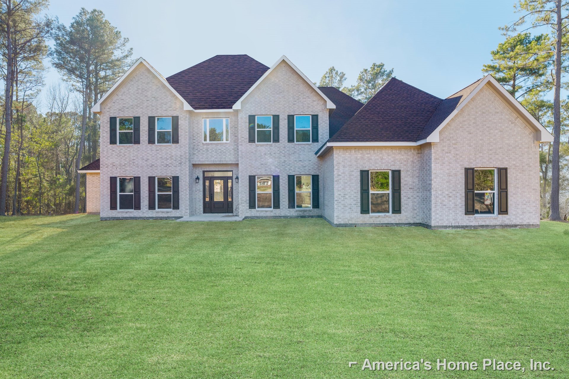 White farmhouse-style home with green shutters, expansive front lawn, mature trees, brick accents, and large windows reflecting surrounding greenery
