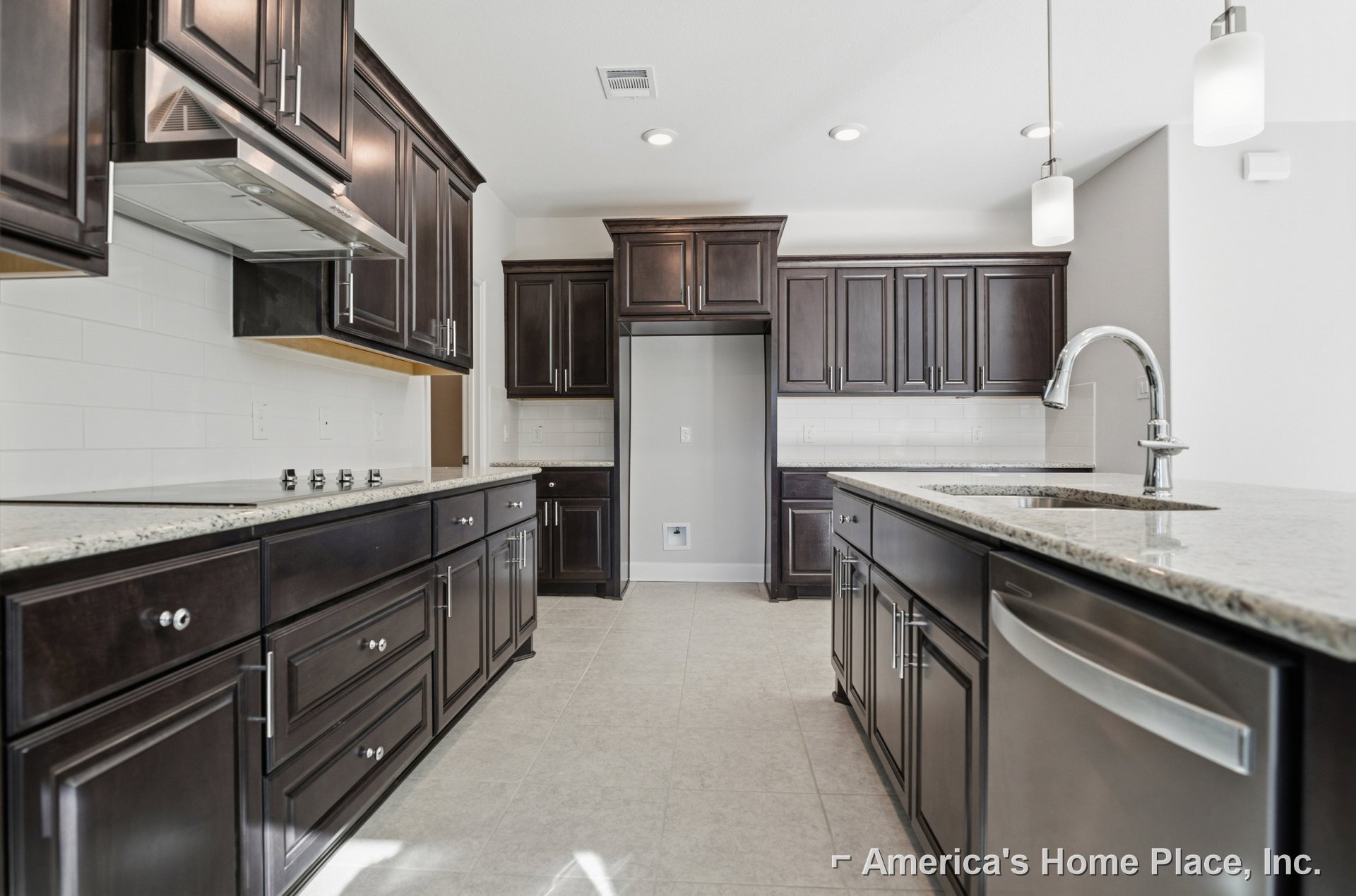 Kitchen with dark wood cabinets, white tile floor, stainless steel dishwasher, white walls, ceiling vent, and sink on dark countertop