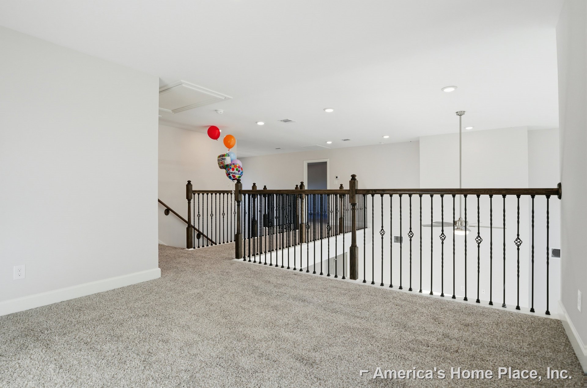 Curved staircase with wooden steps and metal railing, white plaster walls, light hardwood flooring, and a decorative balloon with text near the entryway