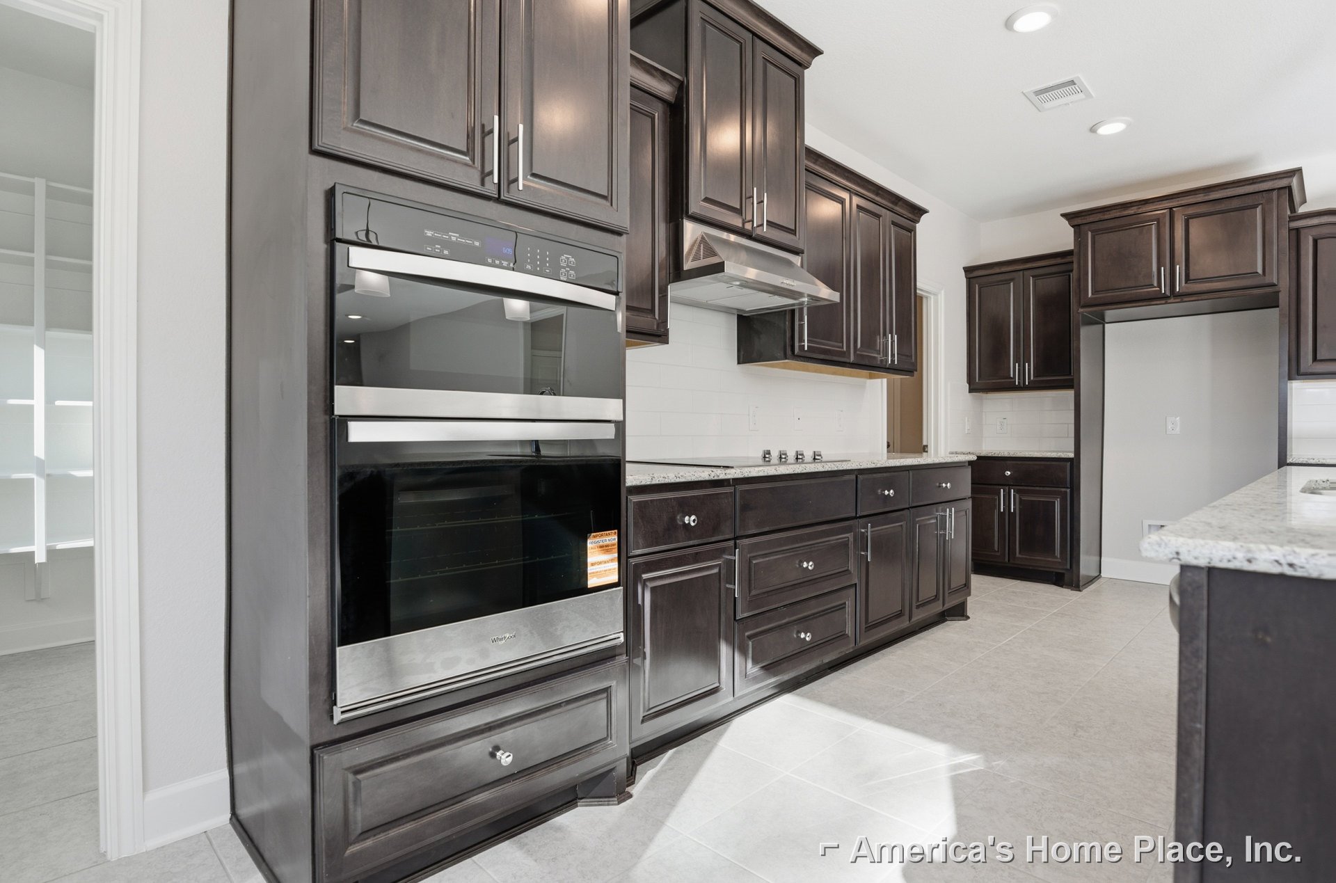 Kitchen featuring dark wood cabinets, stainless steel oven with glass door, built-in microwave, white wall with electrical outlet, and sleek drawer fronts