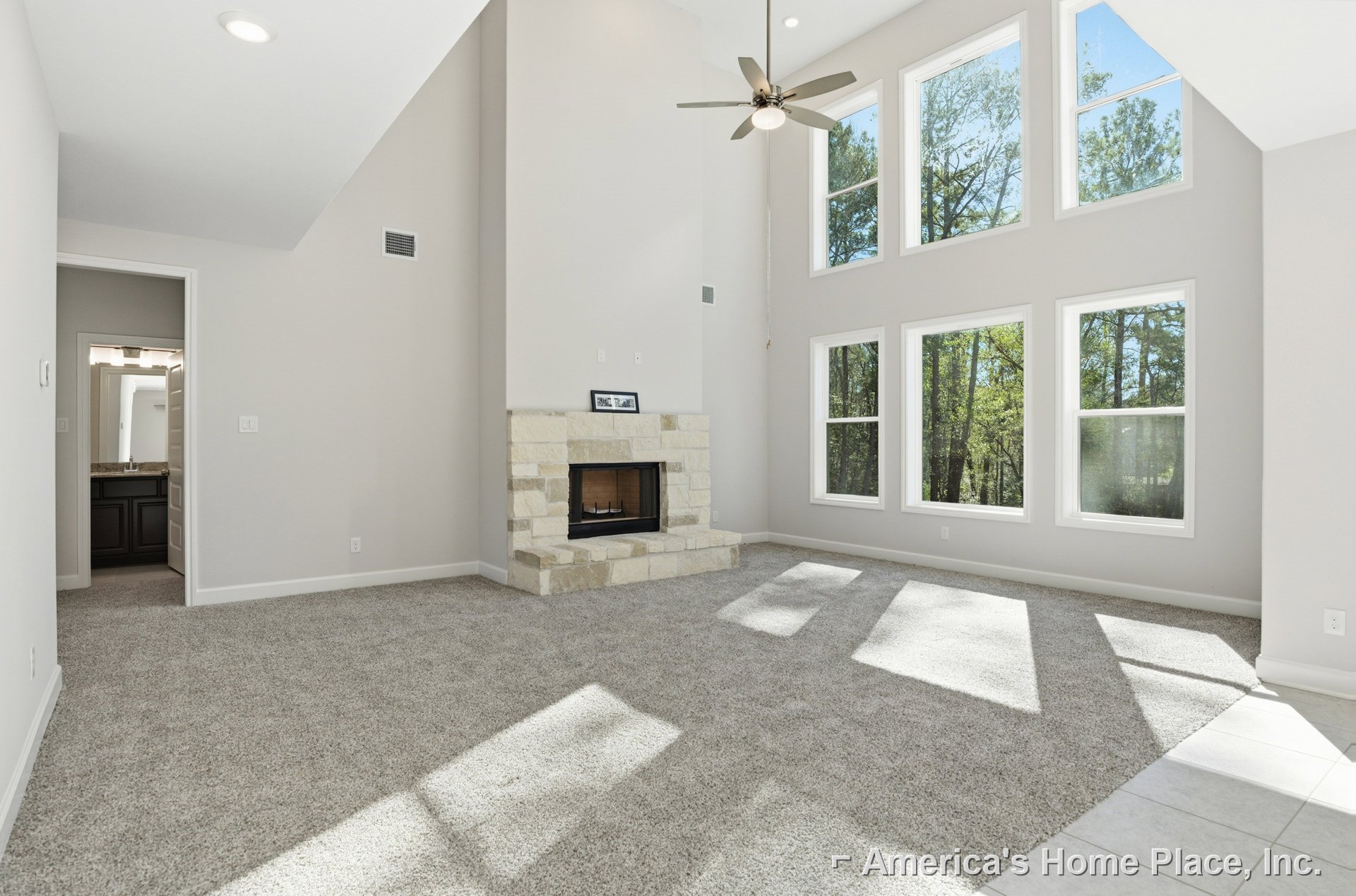 Carpeted living room featuring a tile fireplace with a picture frame above, ceiling fan with light, and window overlooking trees