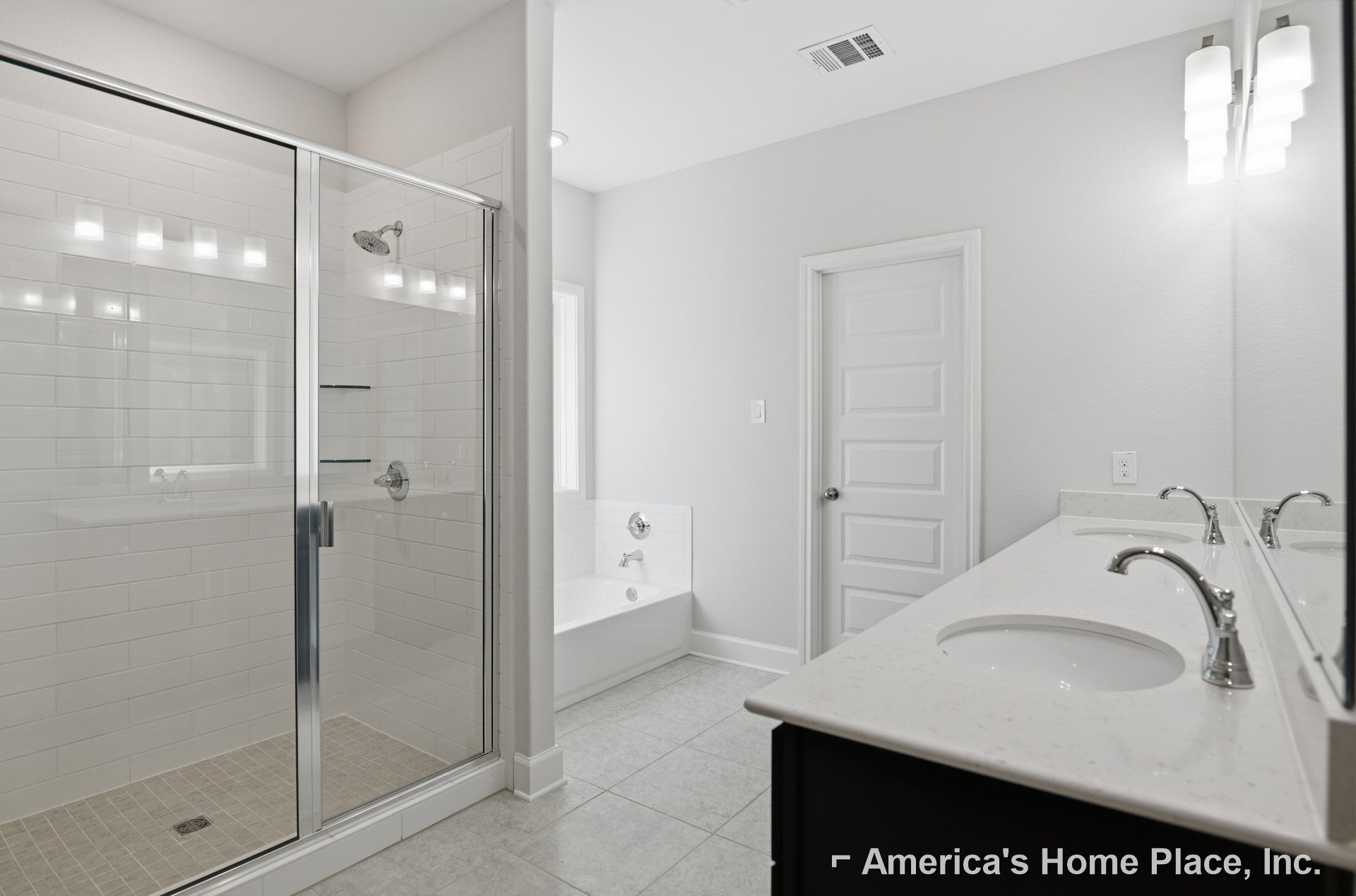 Modern bathroom featuring a glass-enclosed shower, white vanity with chrome faucets, wall-mounted light fixture, and a white door with silver hardware.