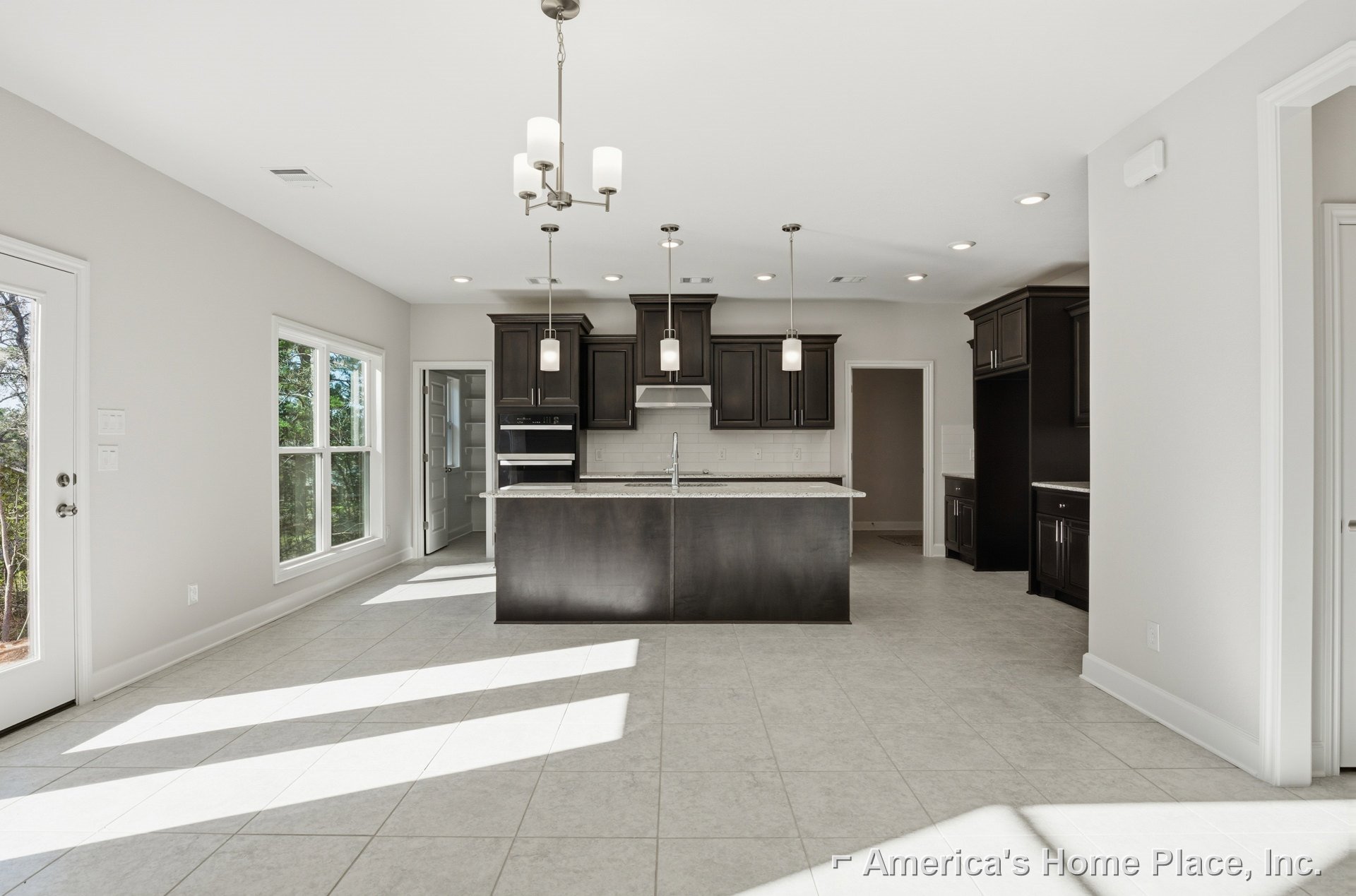 Spacious kitchen featuring two islands with white countertops, tile flooring, white cabinetry, stainless steel sink, large window overlooking trees, and white door with glass panel